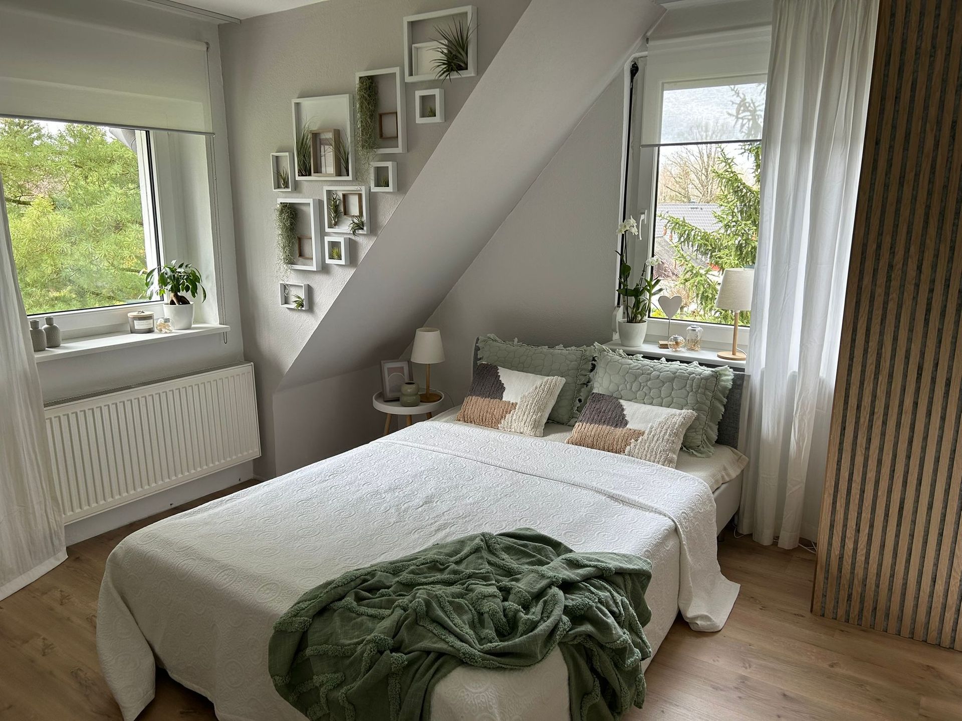 Bright bedroom with a white bed, green throw, striped accent wall, and windows showing greenery.