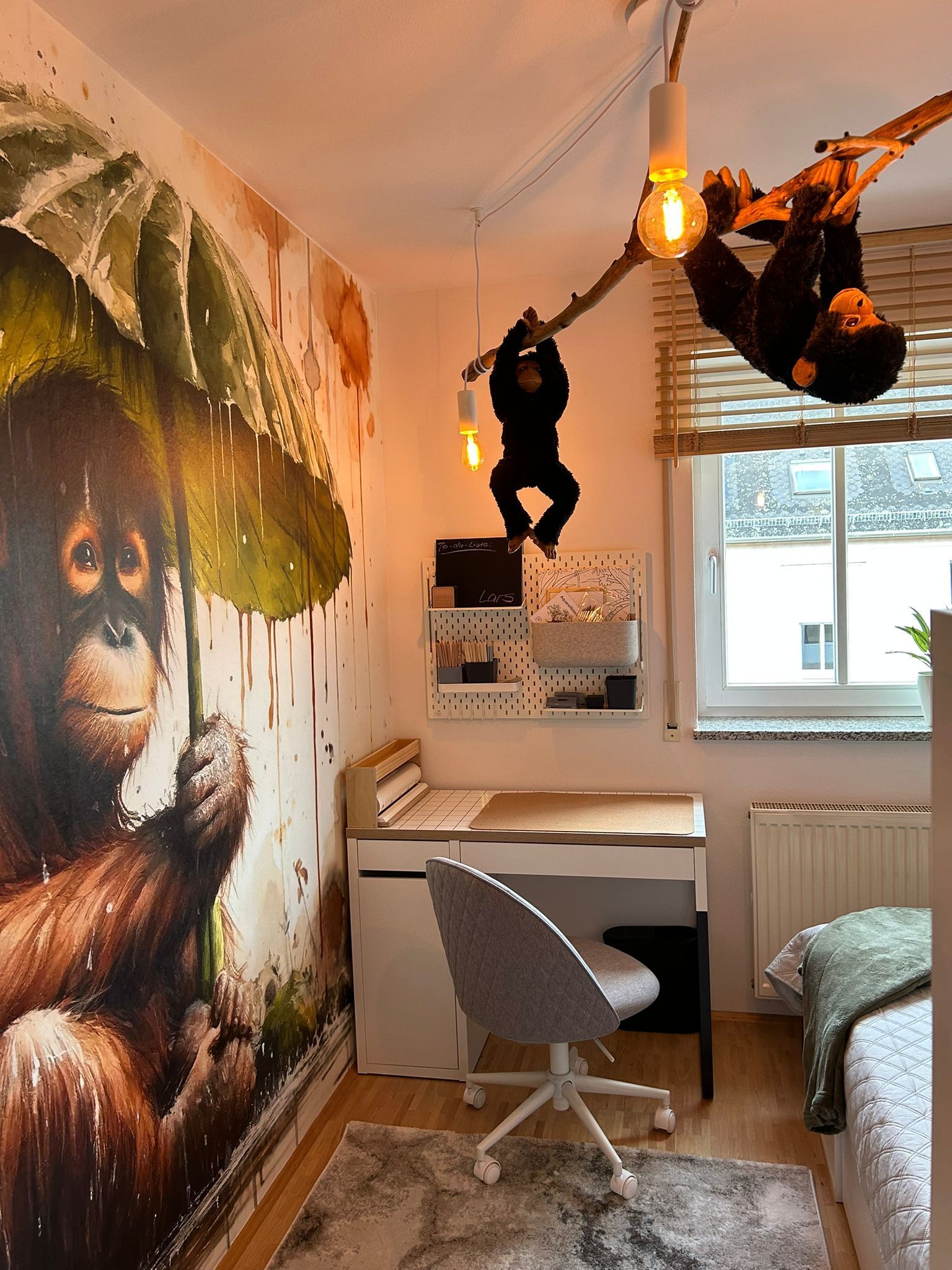 Kleines Zimmer mit Orang-Utan-Wandbild, hängender Affendekoration, Schreibtisch, Stuhl, Fenster und Etagenbett
