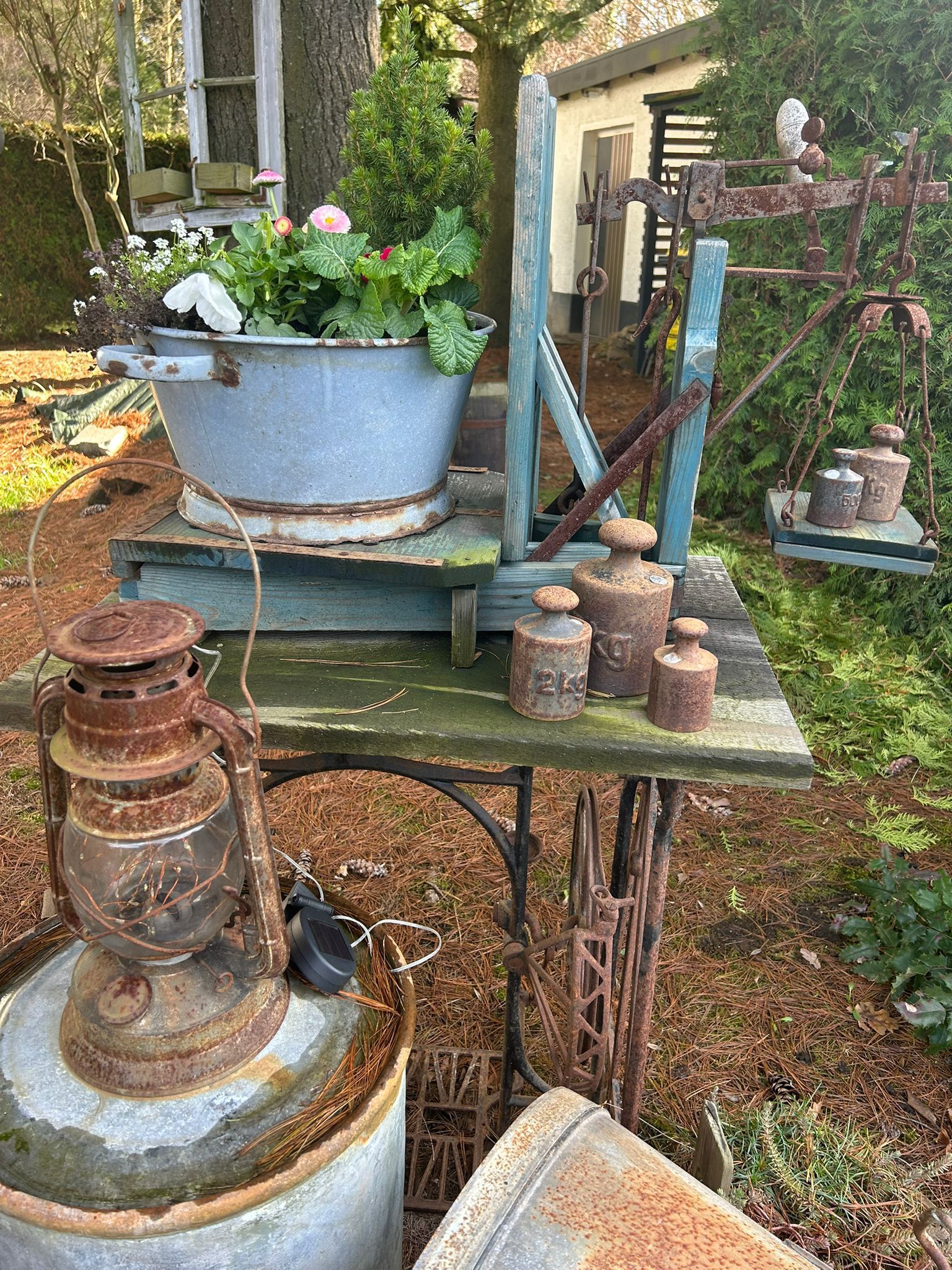 Rustic garden display with potted plants, old lanterns, and stacked clay pots on a weathered table