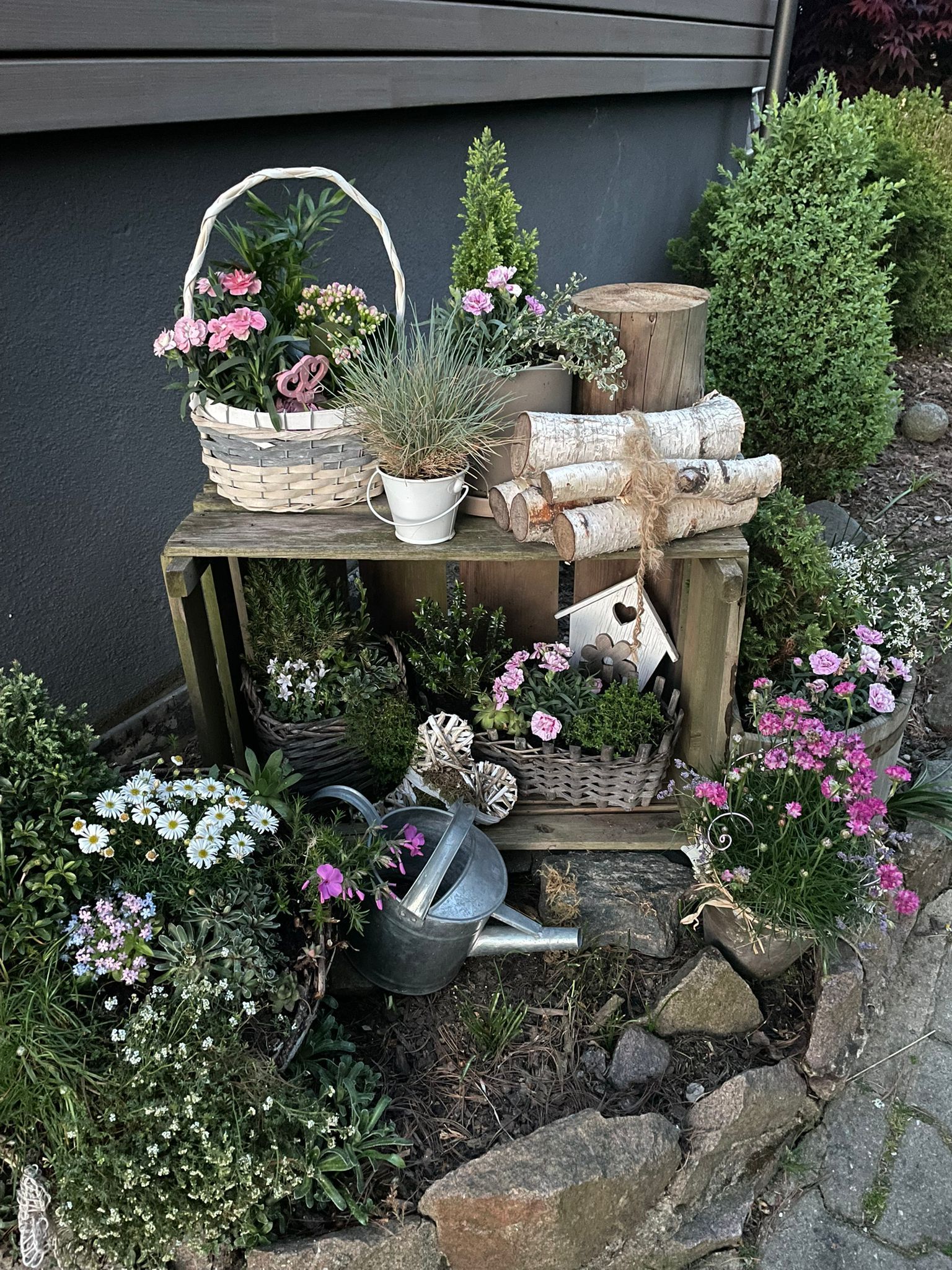 Kleiner, rustikaler Gartenbereich mit Topfblumen, gestapelten Ziegelsteinen und Grünpflanzen neben einer Hauswand
