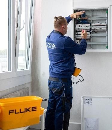 Elektriker der ATRA TEC GmbH prüft einen Verteiler mit einem Fluke-Messgerät