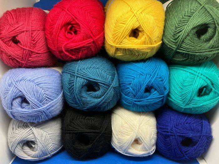 12 Knäuel Sockenwolle uni in den Farben des Regenbogens und in schwarz, weiß und grau.
