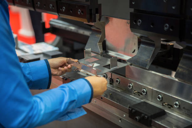 Ein Arbeiter in blauer Arbeitskleidung richtet ein Blechteil in einer industriellen Abkantpresse für einen Biegevorgang aus.