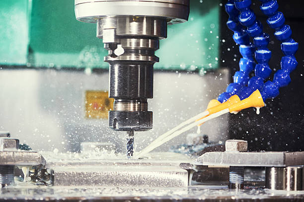Eine CNC-Fräsmaschine bearbeitet ein Metallwerkstück, während sie durch einen Flüssigkeitsstrahl aus einer blauen Düse gekühlt wird.