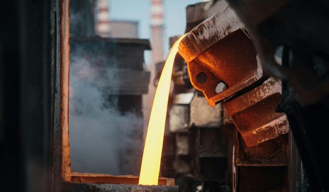 In einer Gießerei fließt geschmolzenes Metall aus einer glühenden, robusten Industriegießpfanne in eine Gussform.