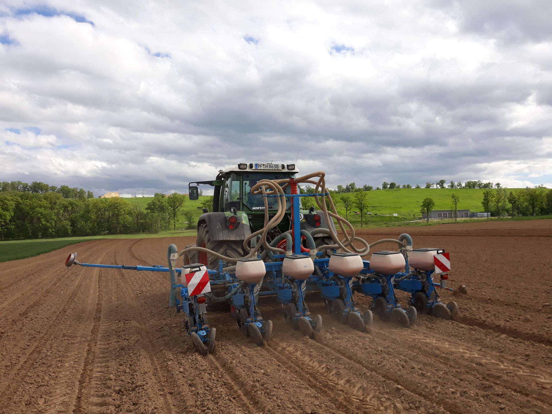 Fendt-Traktor mit Monosem-Einzelkornsägerät bei der Aussat, im Hintergrund eine grüne Hügellandschft unter wolkigem Himmel.