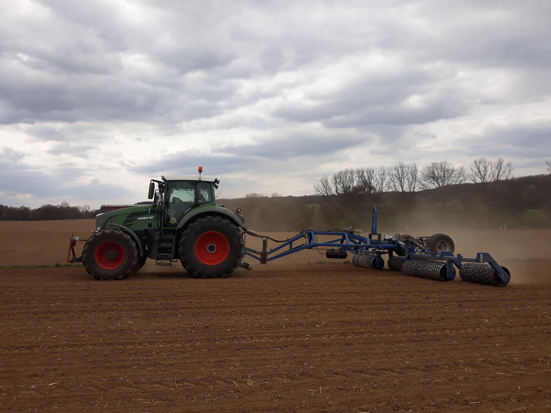 Fendt-Traktor mit angehänter Dalbo-Walze beim Befahren eines Ackerfeldes unter bewölktem Himmel.