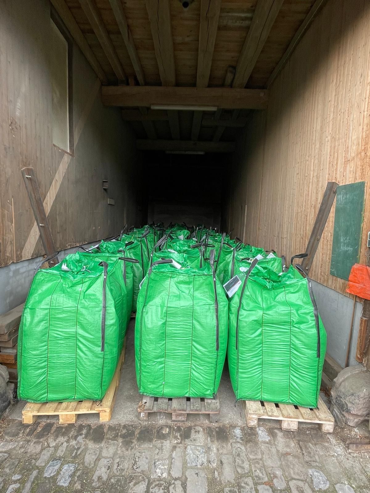 Grüne Bigbags auf Paletten in einer Lagerhalle.