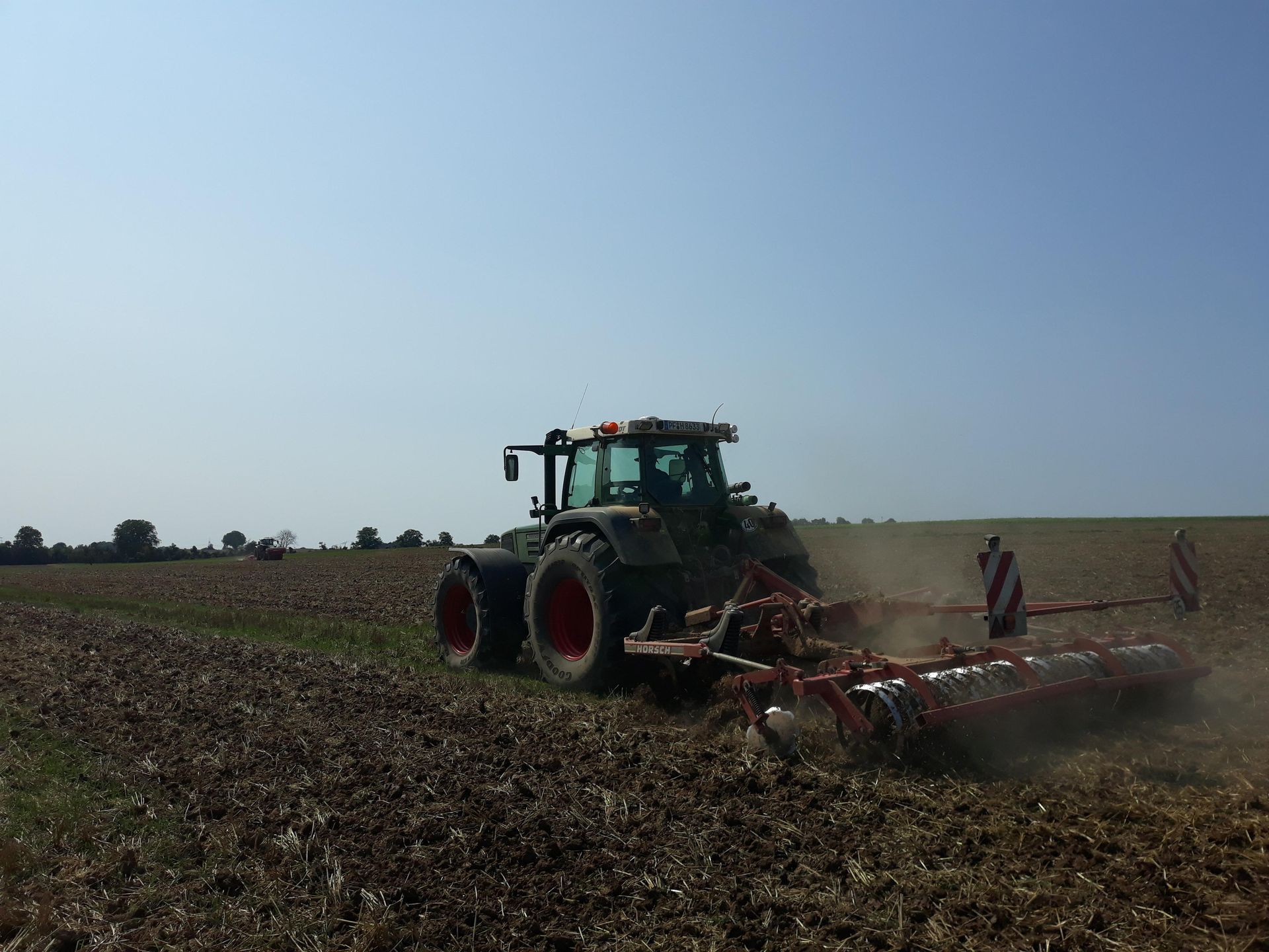 Fendt-Traktor mit Horsch-Grubber beim Arbeiten auf dem Acker unter klarem Himmel. 