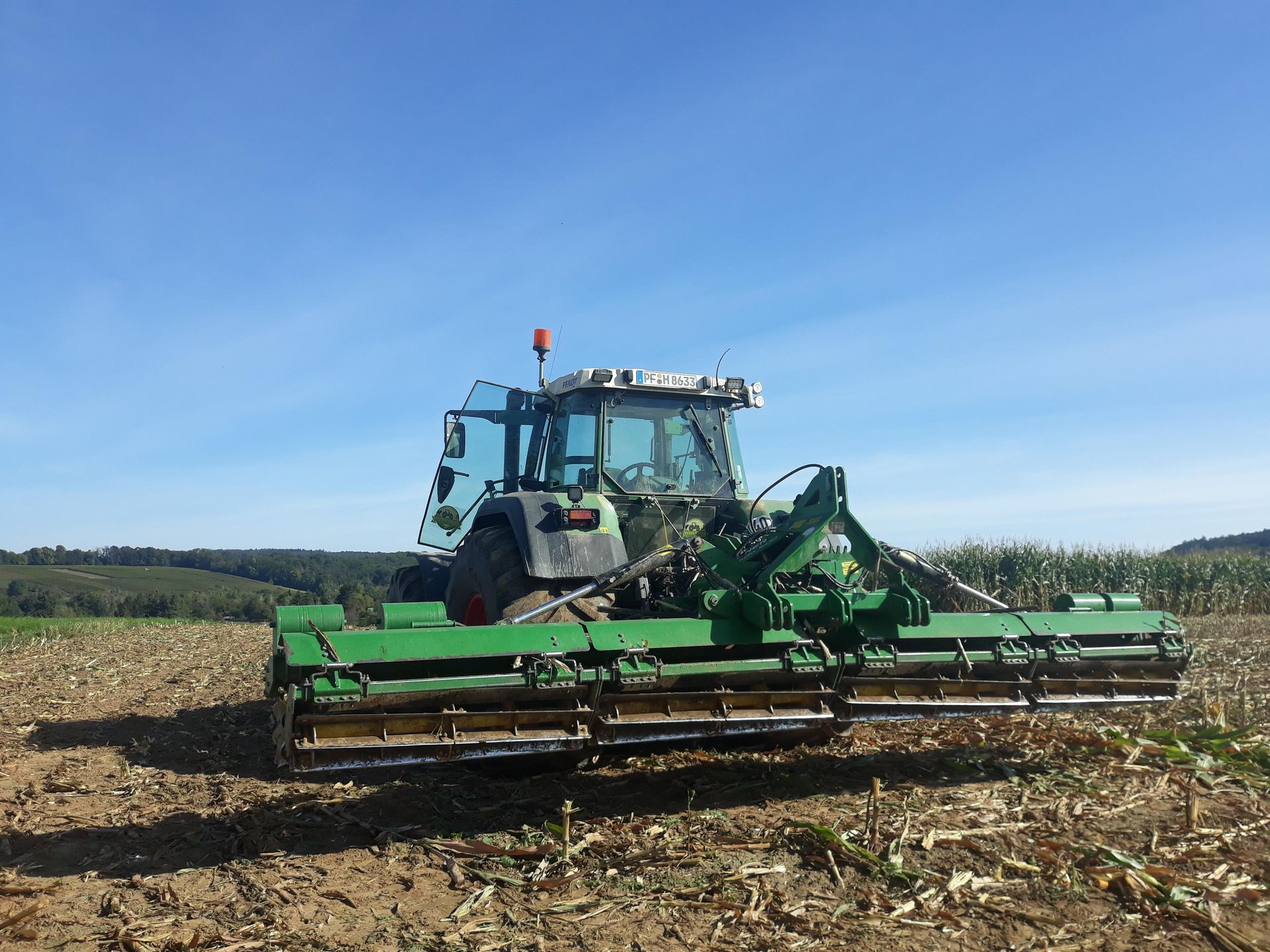 Fendt-Traktor mit angehänter Kerner-Walze nach dem bearbeiten der Rapsstoppel auf dem Feld, unter blauem Himmel.