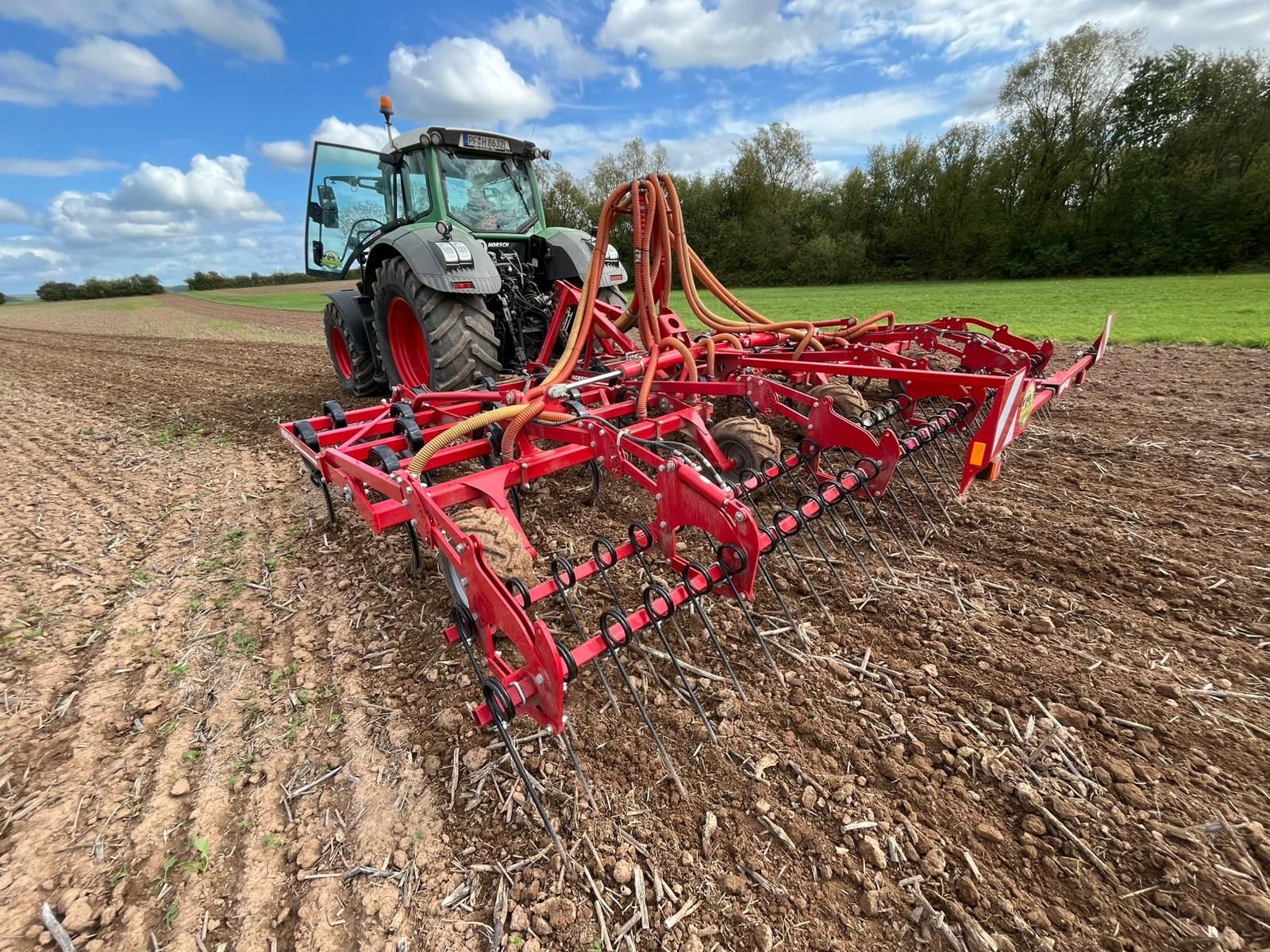 Fendt-Traktor mit angebautem Leichtgrubber bei der Bodenbearbeitung auf einem Acker unter blauem Himmel.