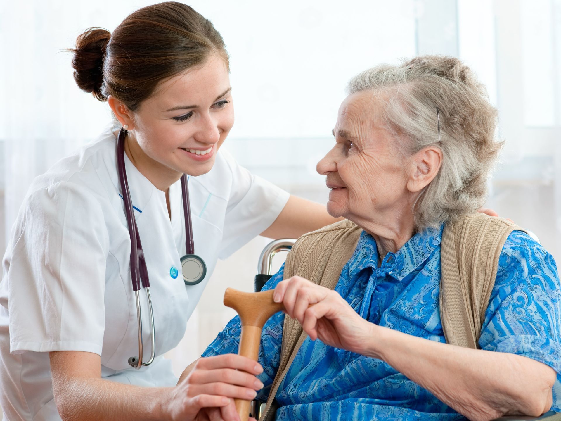 In einer hellen Klinik lächelt eine Krankenschwester und unterhält sich mit einem älteren Patienten, der einen Rollator benutzt.