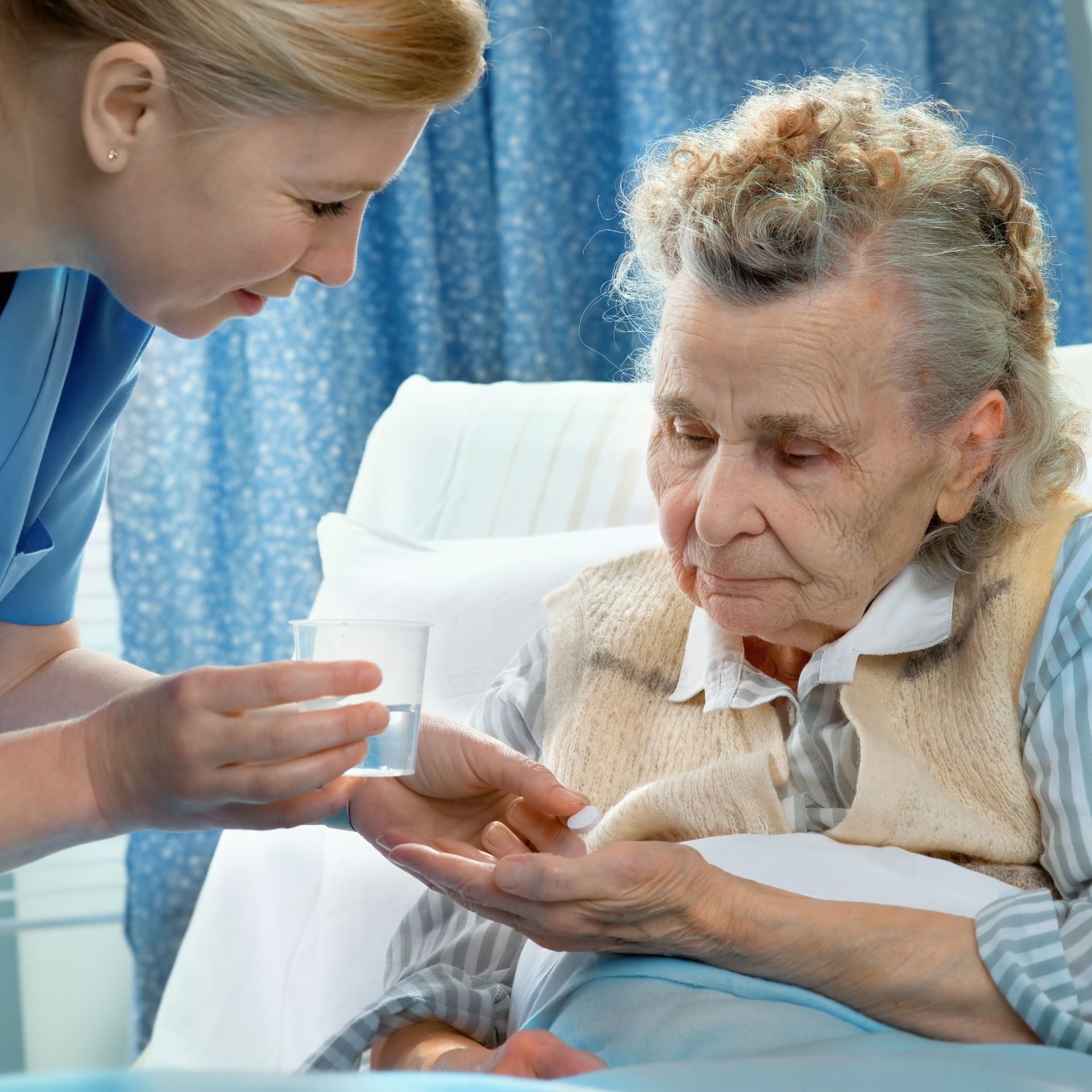 Eine Pflegekraft reicht einem älteren Patienten im Krankenhausbett eine Pille.