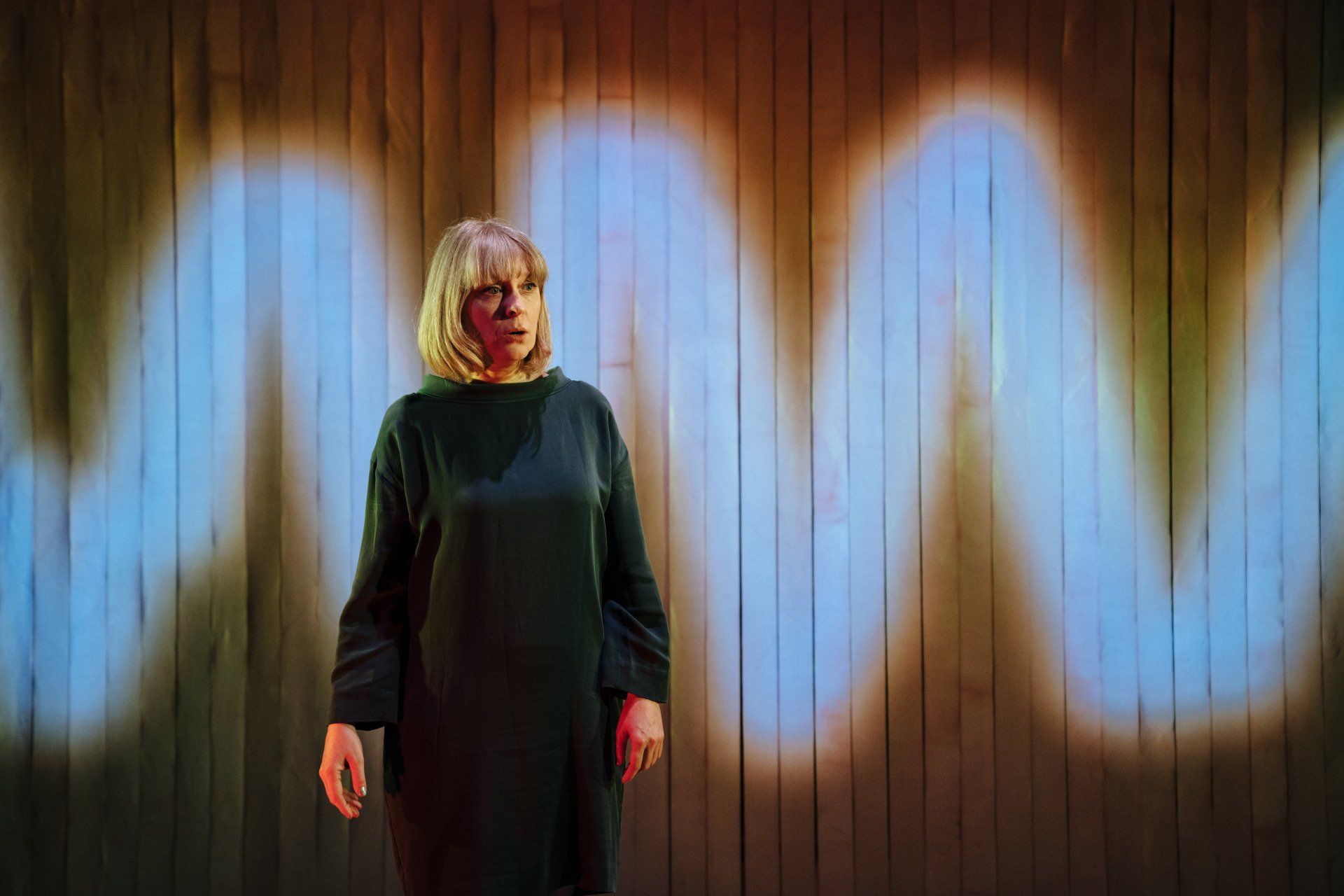 Sophie the performer stands on a stage looking amazed and curious, listening. We see a giant white sound wave projected onto the set behind her