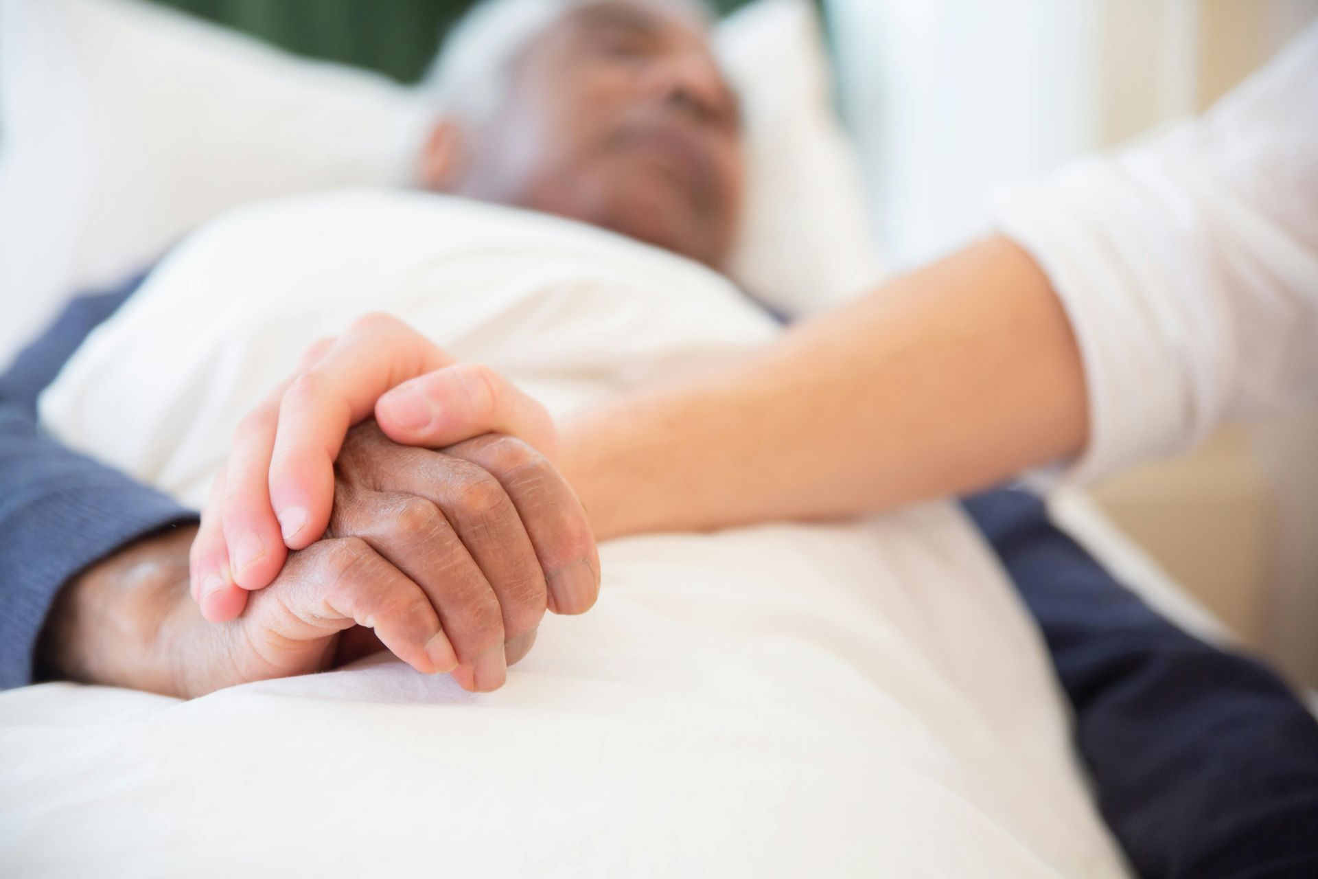 Hand hält liebevoll die eines älteren Menschen im Krankenbett