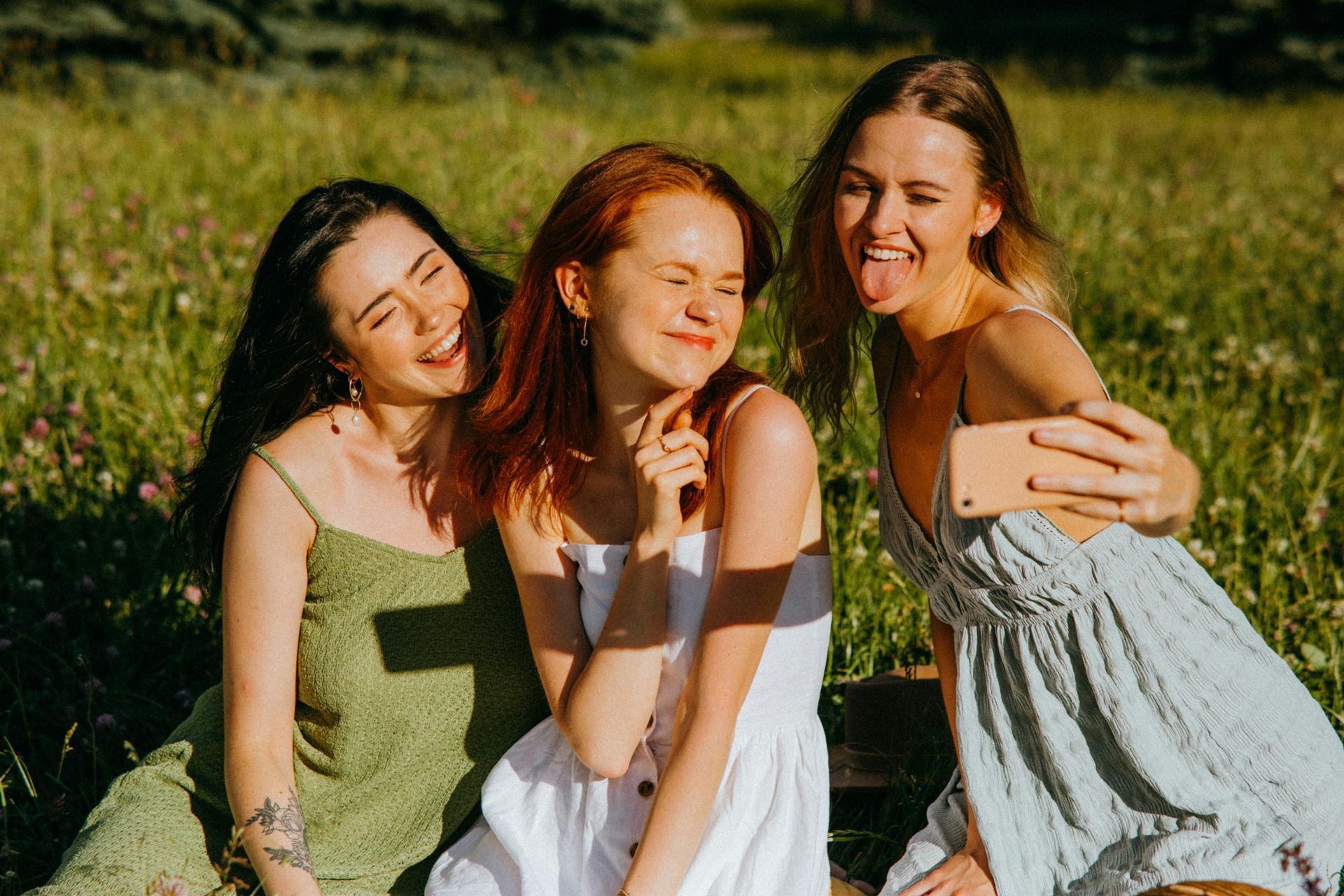 Drei junge Frauen machen lachend ein Selfie auf einer Wiese
