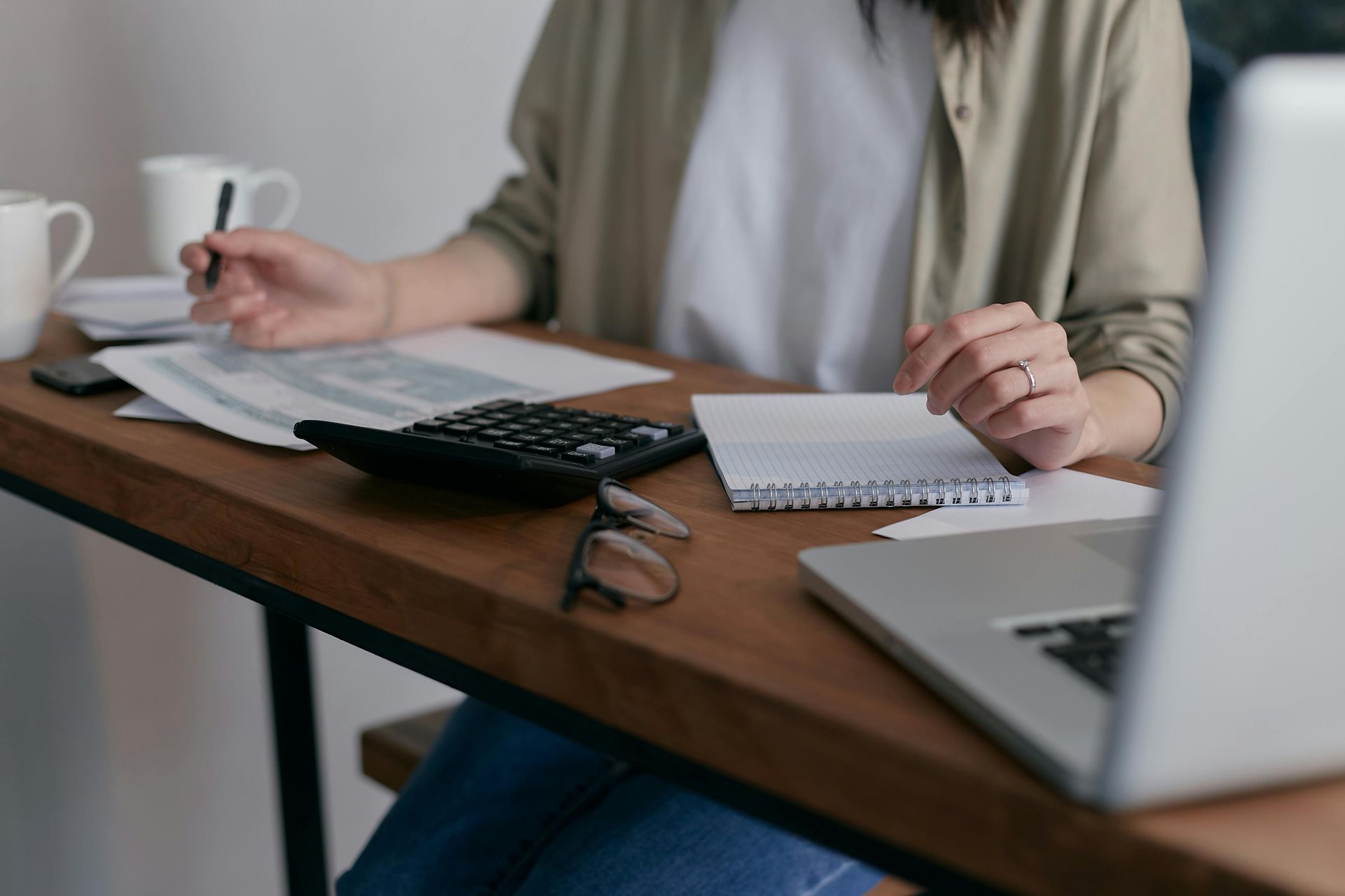 Person arbeitet mit Laptop, Taschenrechner und Notizblock