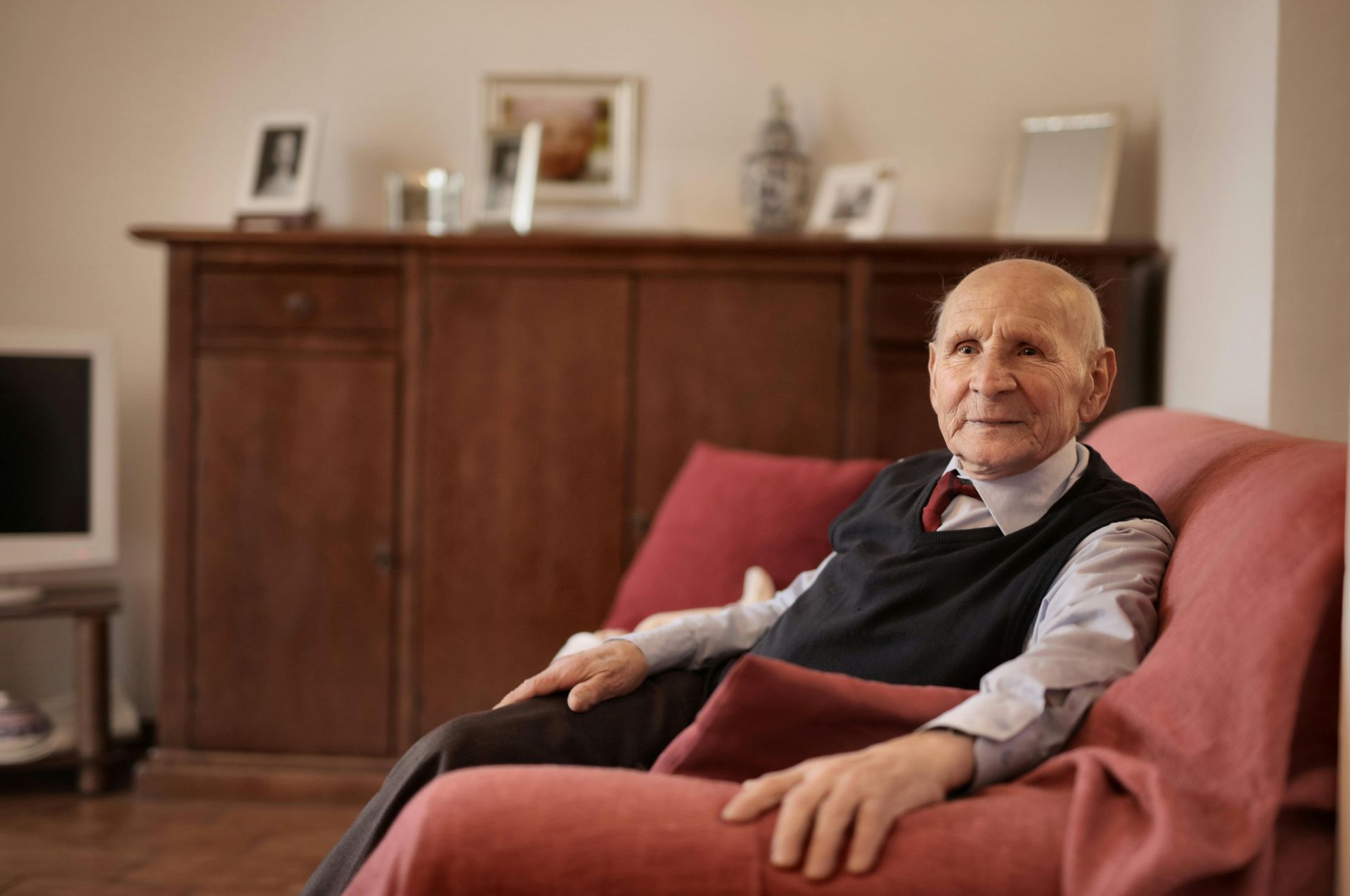 Älterer Mann sitzt ruhig auf einem roten Sofa im Wohnzimmer