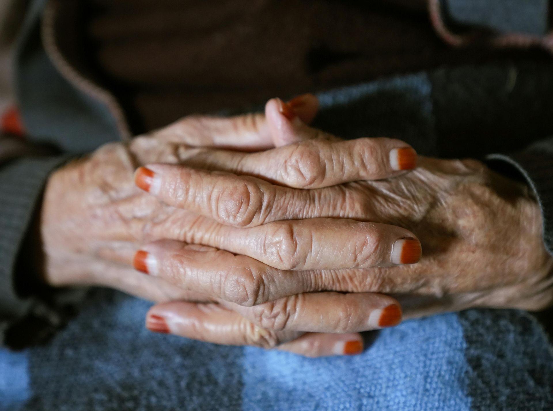 Gefaltete Hände einer älteren Person mit lackierten Fingernägeln