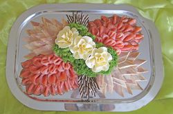 Silberne Platte mit arrangierten Räucherlachsscheiben, Zierblumen und Stäbchen auf einer grünen Tischdecke.