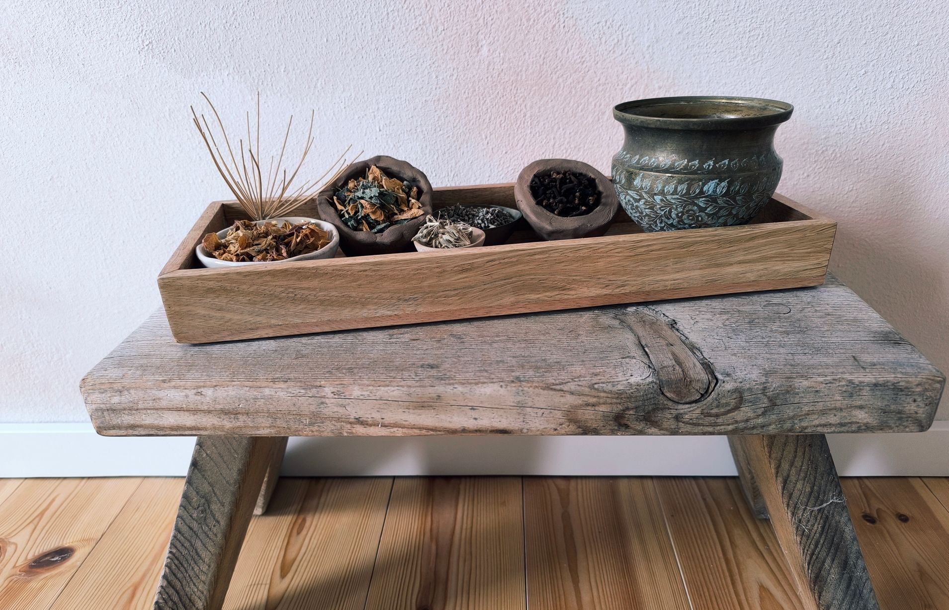 Ein Holzbänkchen mit einem Holztablett, darauf stehen kleine Schälchen mit Räucherwerk angeordnet.