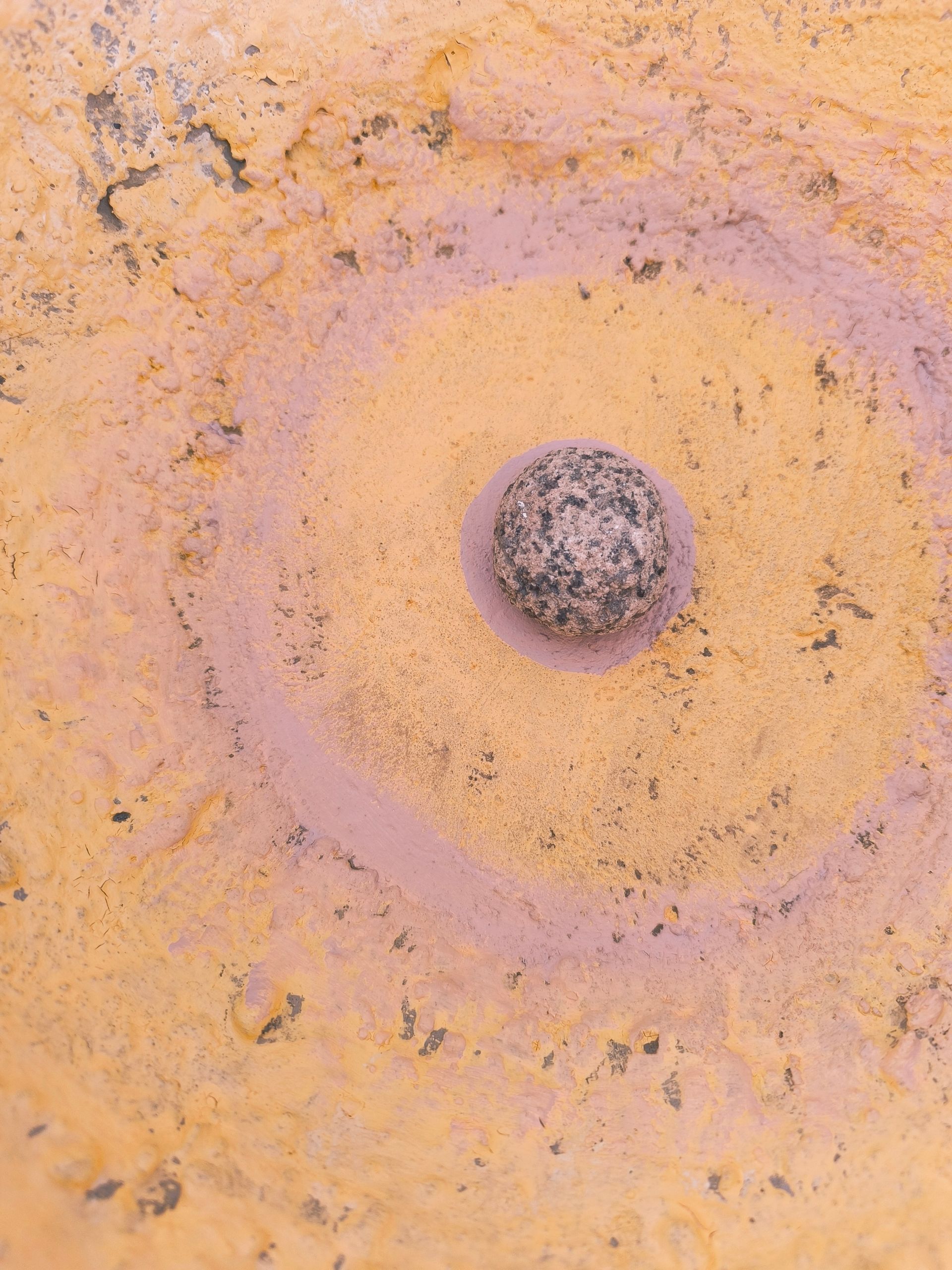 Nahaufnahme einer gelbenBetonschale, in der ein runder Stein auf dem Boden der Schale liegt.