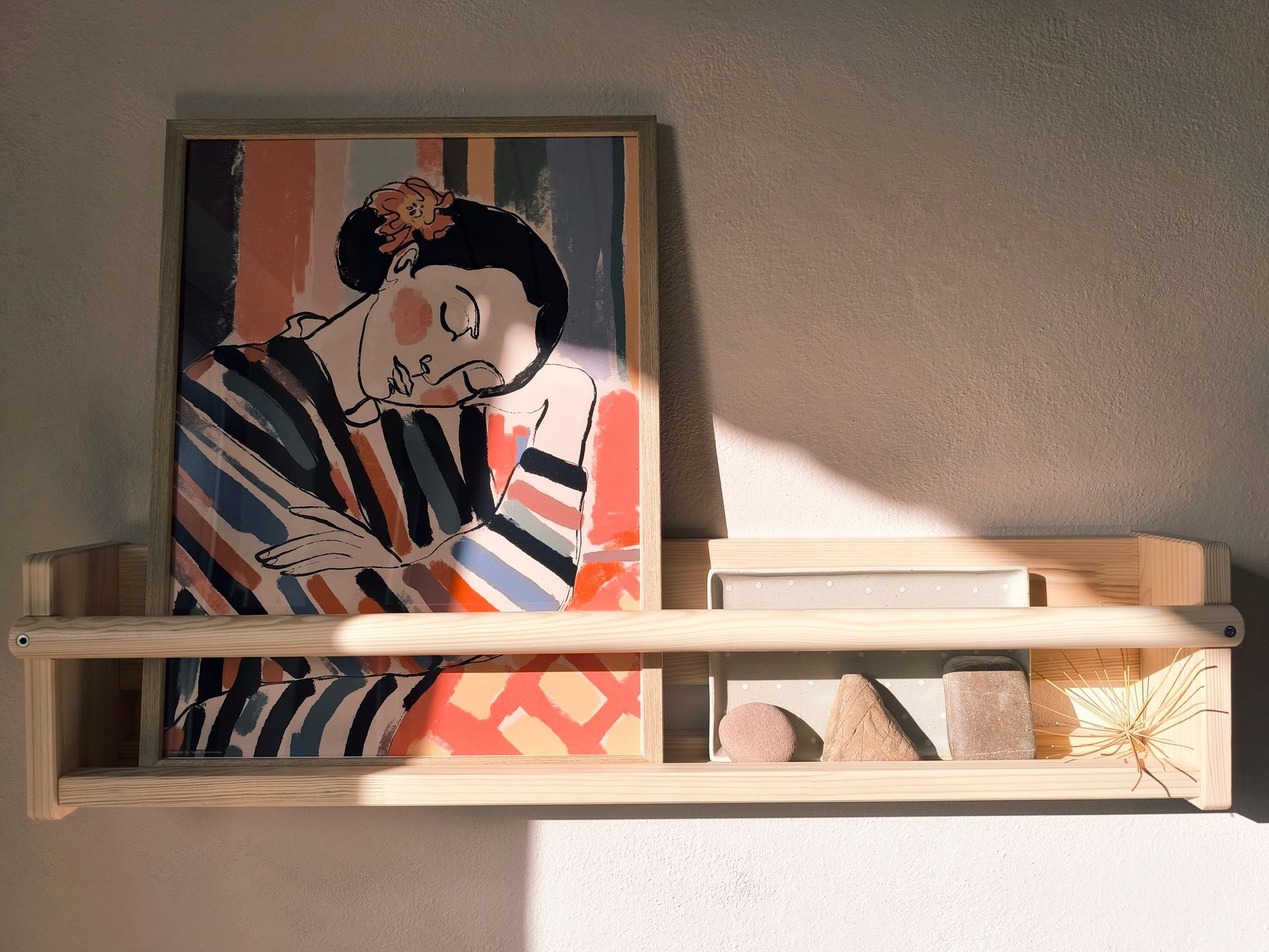 Ein Wandregal mit einem Bild und drei Steinen, es wird von der Sonne direkt angestrahlt.