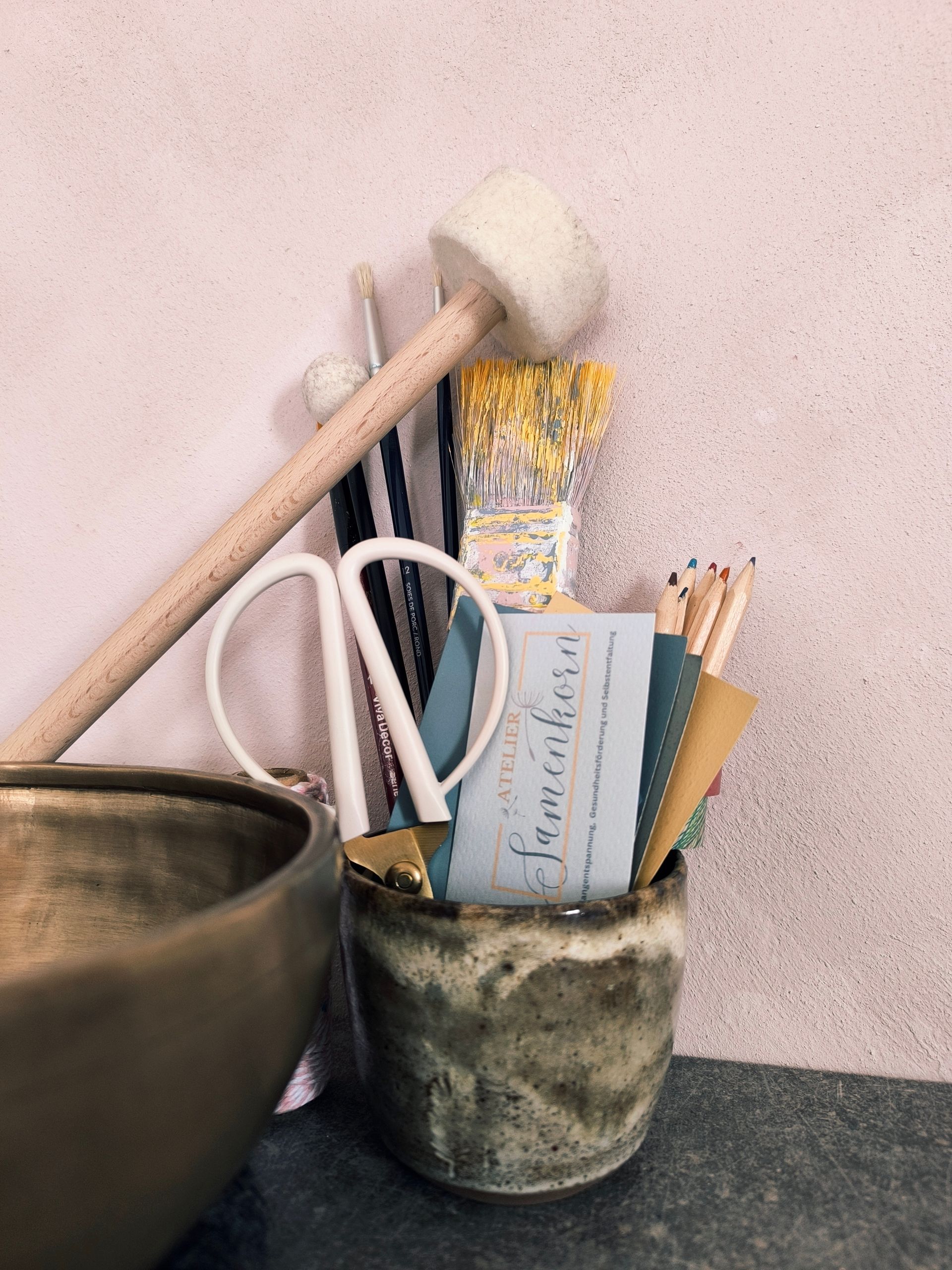 Das Bild zeigt Malutensilien in einem Behälter und eine Klangschale daneben. Sie stehen für den Klang und die Kreativität.