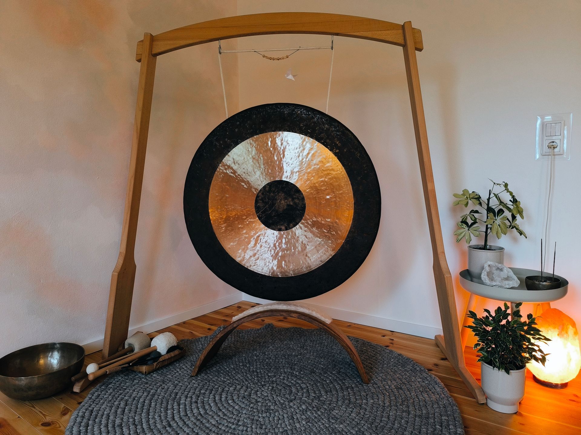 Bildauschnitt vom Entspannungsraum im Atelier Samenkorn. Großer Gong hängt am Ständer, rechts leuchtet eine Salzlampe.