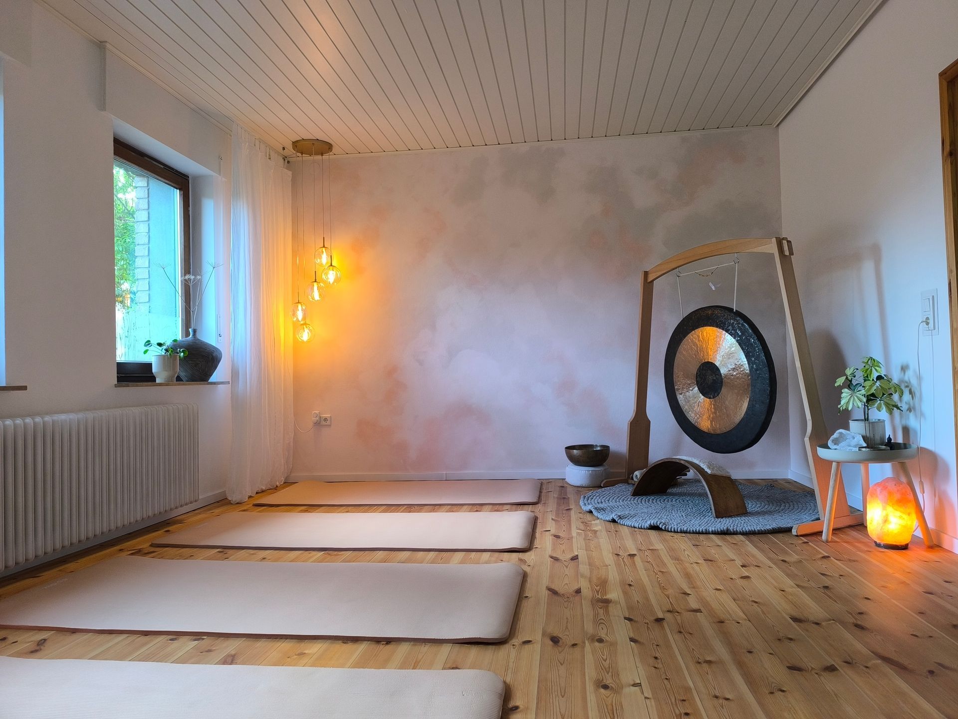 Der Entspannungsraum im Atelier Samenkorn. Ein Raum mit zwei Fenstern, einem Holzboden und einem Großen Gong im Raum.