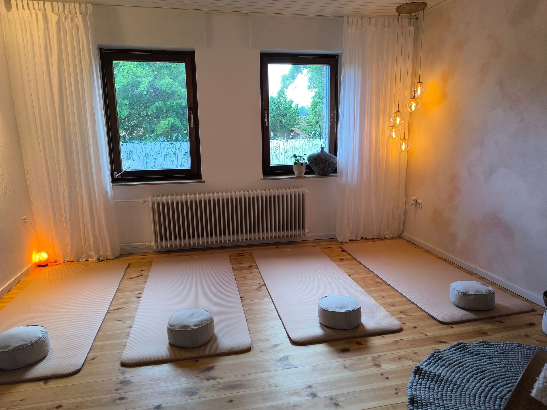 Entspannungsraum des Ateliers. Vorbereitet mit Yogamatten und Yogakissen auf dem Boden. Rechts und links sind Lichtquellen.