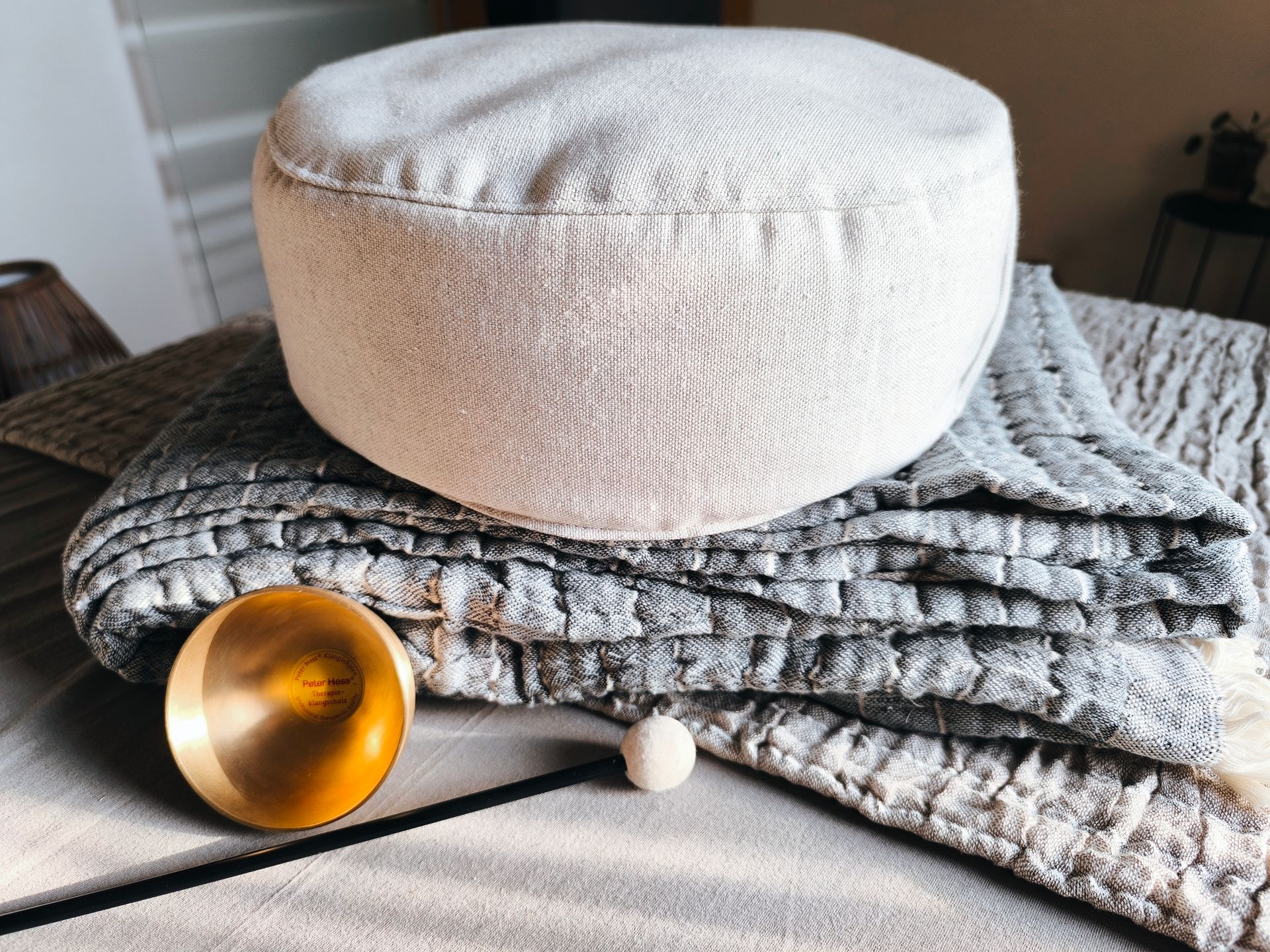 Ein Yogakissen liegt auf einer gefalteten Decke, eine kleine Klangschale steht im Vordergrund.