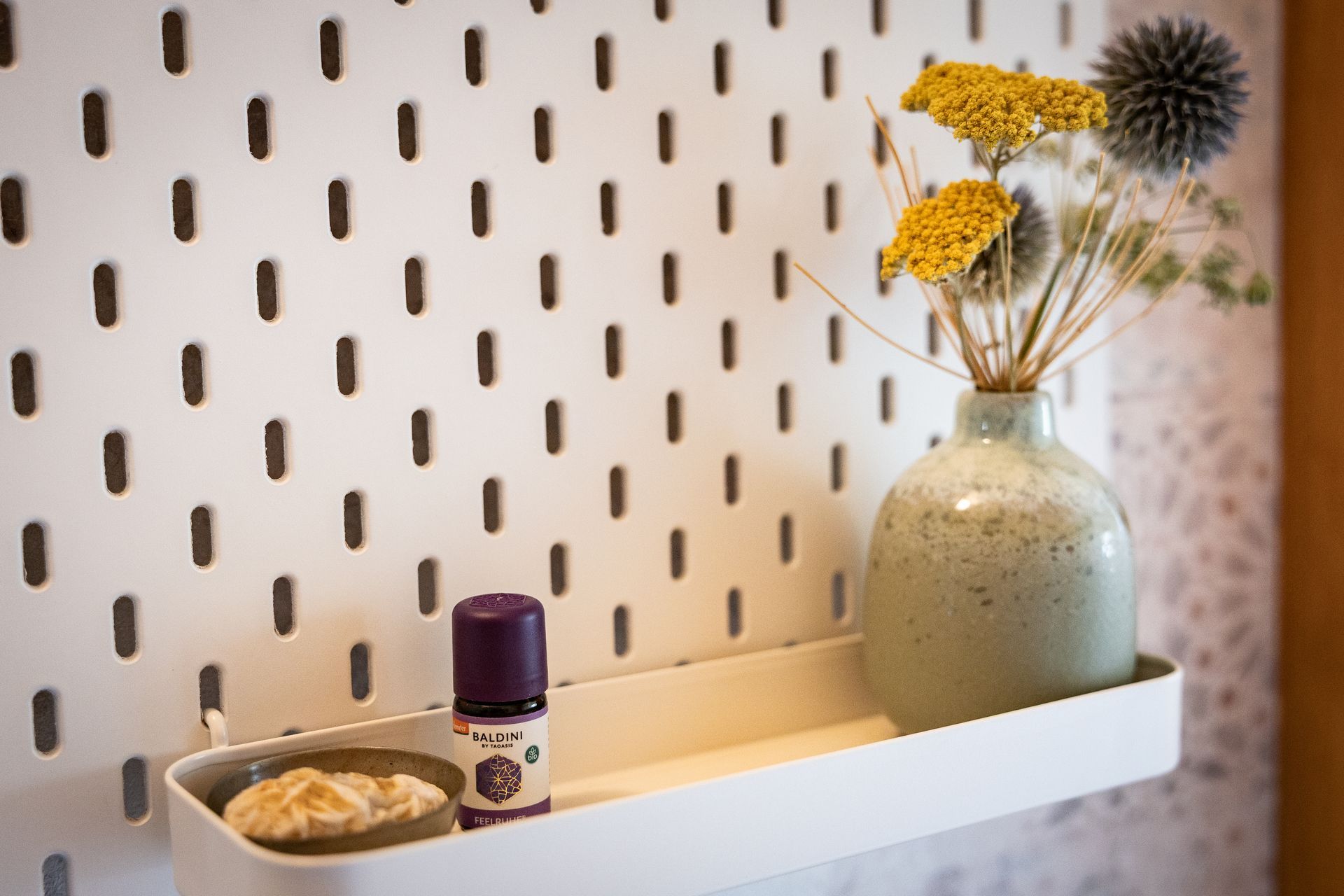 Bildausschnitt vom kleinen Regal mit einer Vase und Trockenblumen. Deko im Eingang des Ateliers.