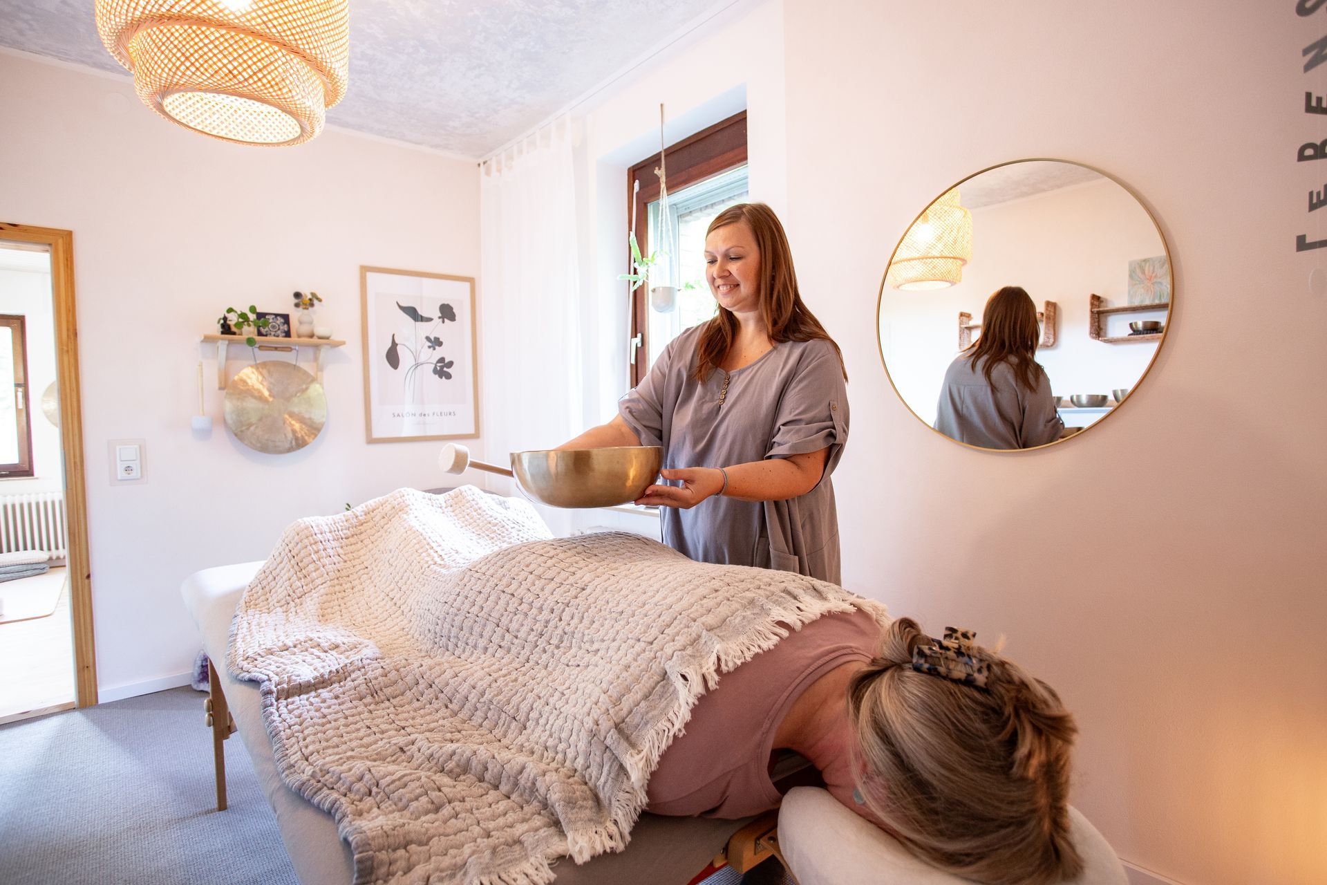 Eine Frau liegt auf einer Massageliege, Julia Pantou hebt eine Klangschale vom Rücken ab.