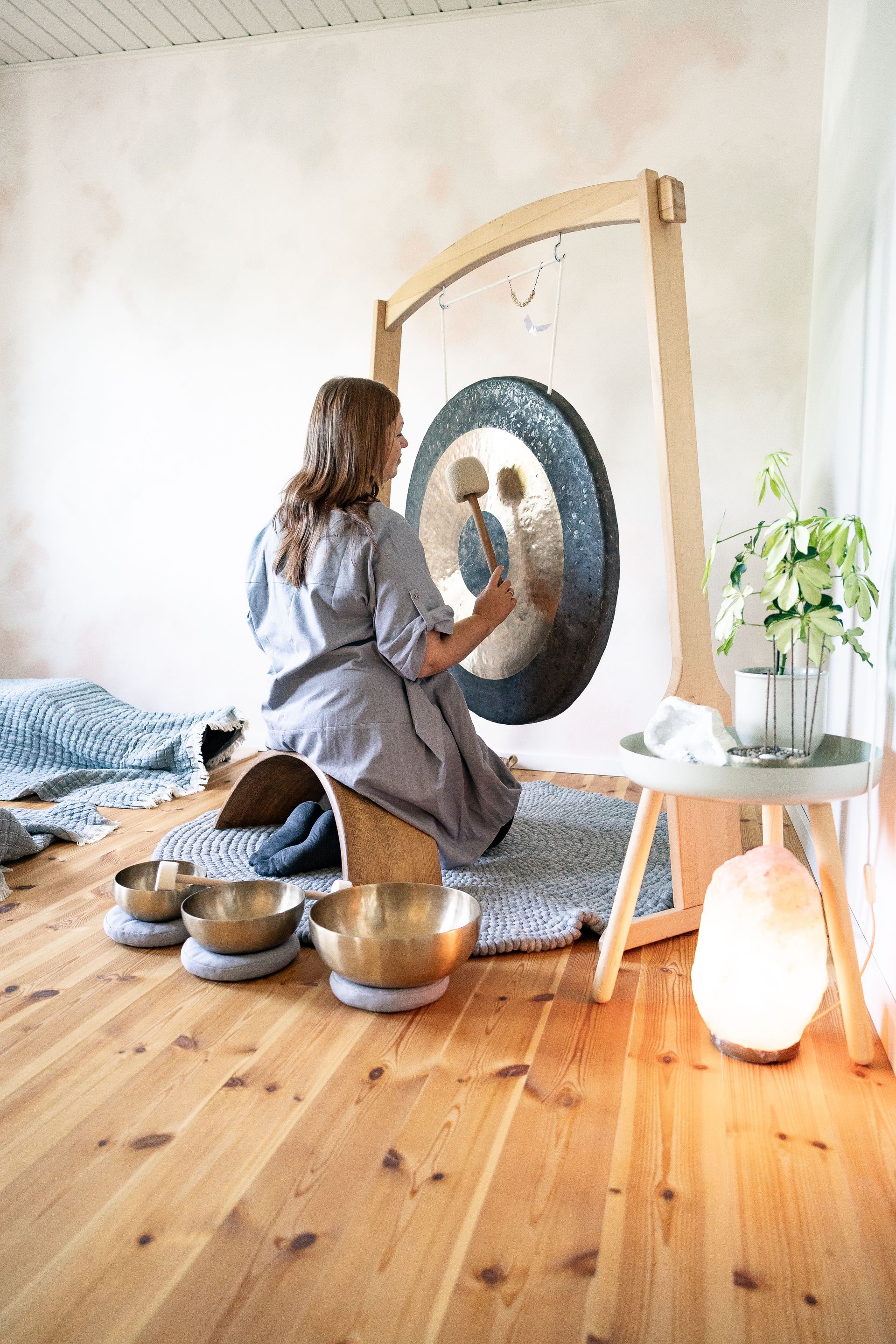 Julia Pantou spielt einen Gong, im Hintergrund liegen zwei Personen zugedeckt auf dem Boden.