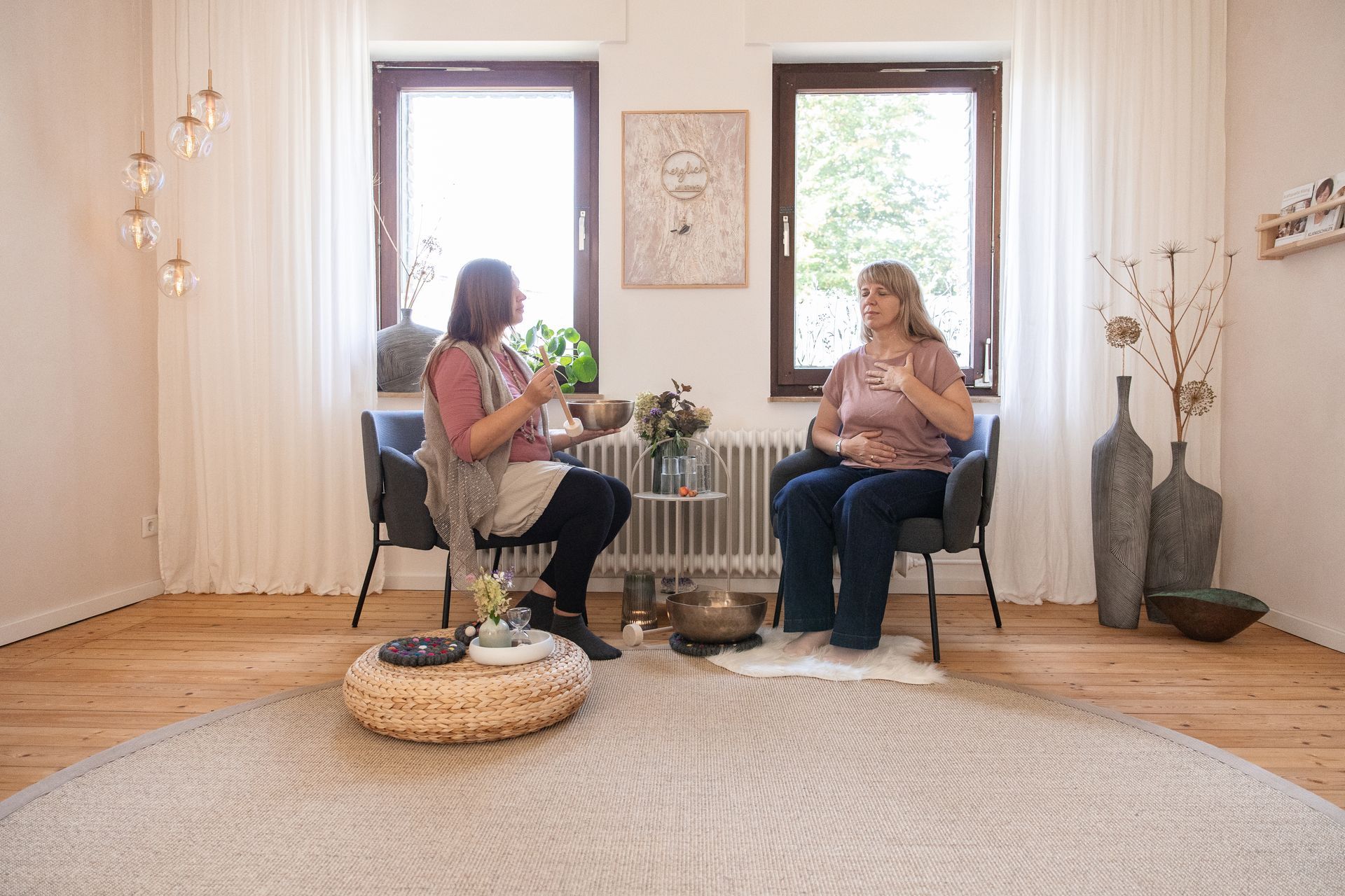 Eine Frau hört auf die Klänge einer Klangschale, die von Julia Pantou angetönt wird. Beide sitzen sich gegenüber. 