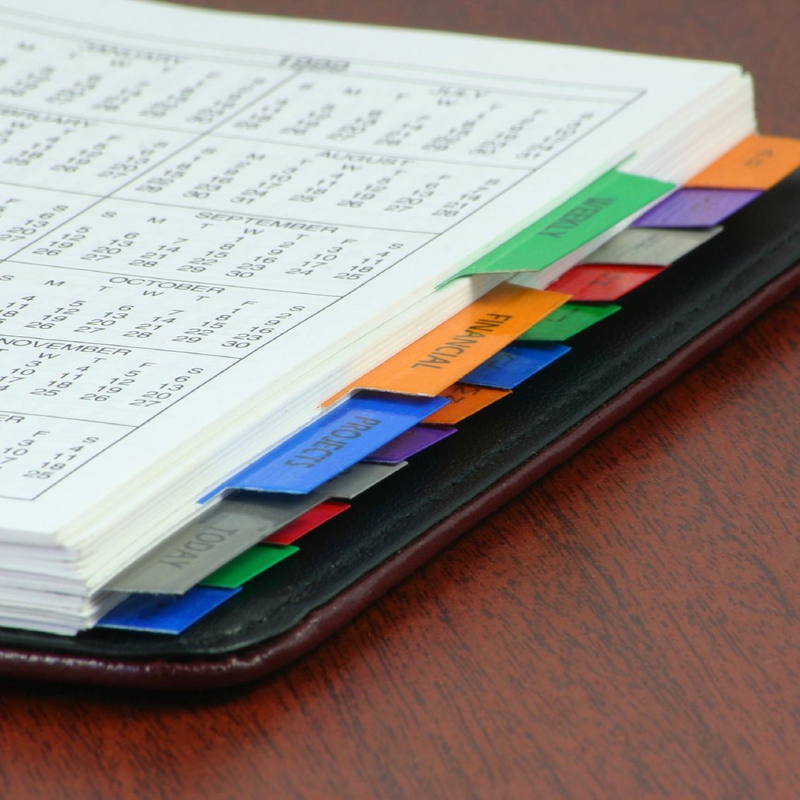 Offenes Notizbuch mit mehrfarbigen Registern auf einer Holzoberfläche.