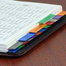 Offenes Notizbuch mit mehrfarbigen Registern auf einer Holzoberfläche.