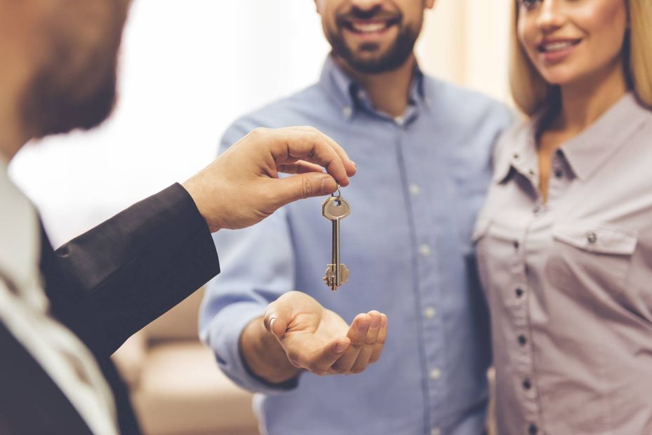 a person handing a set of keys over to a smiling couple