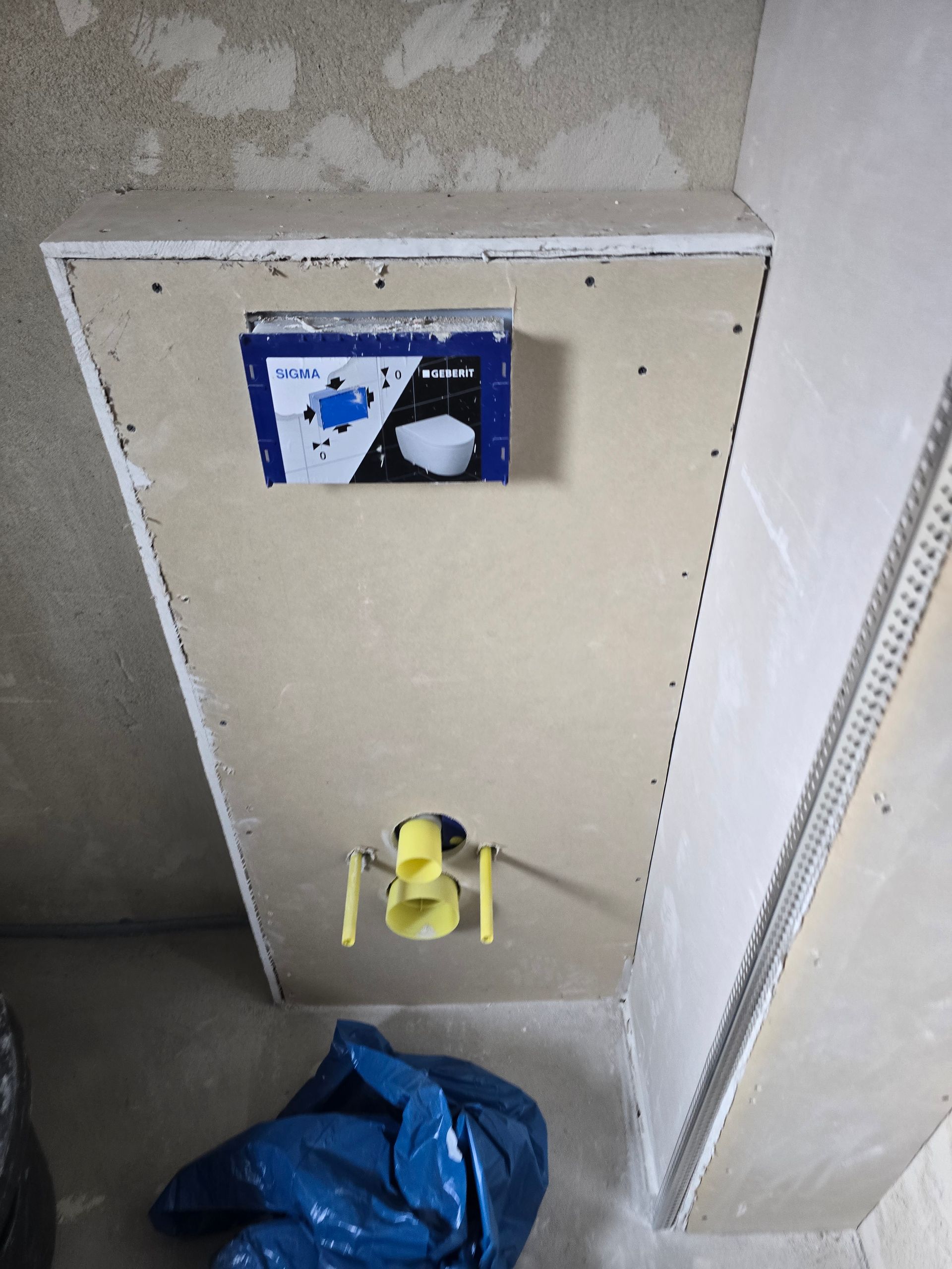 Spülkasten und Spülmechanismus sind in einer teilweise fertiggestellten Wand installiert. Blauer Müllsack auf dem Boden.