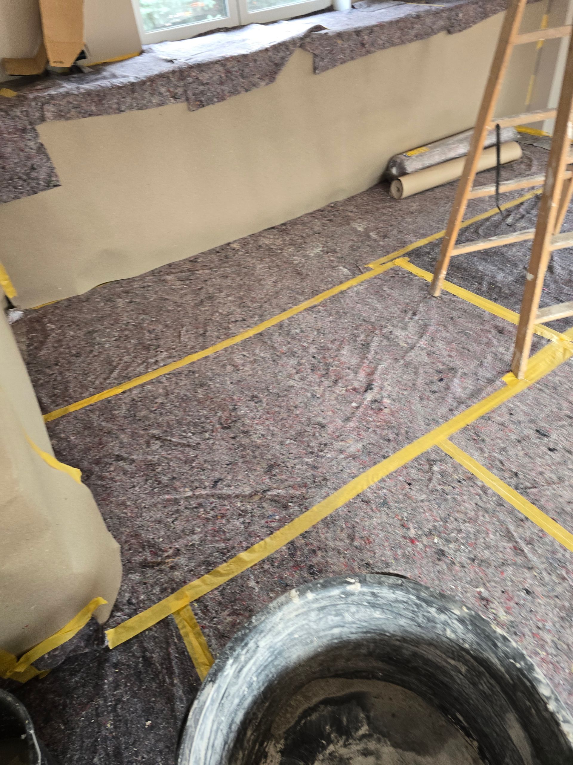 Zimmer wird renoviert, Boden mit Schutzmaterial abgedeckt, Klebeband und eine Leiter.