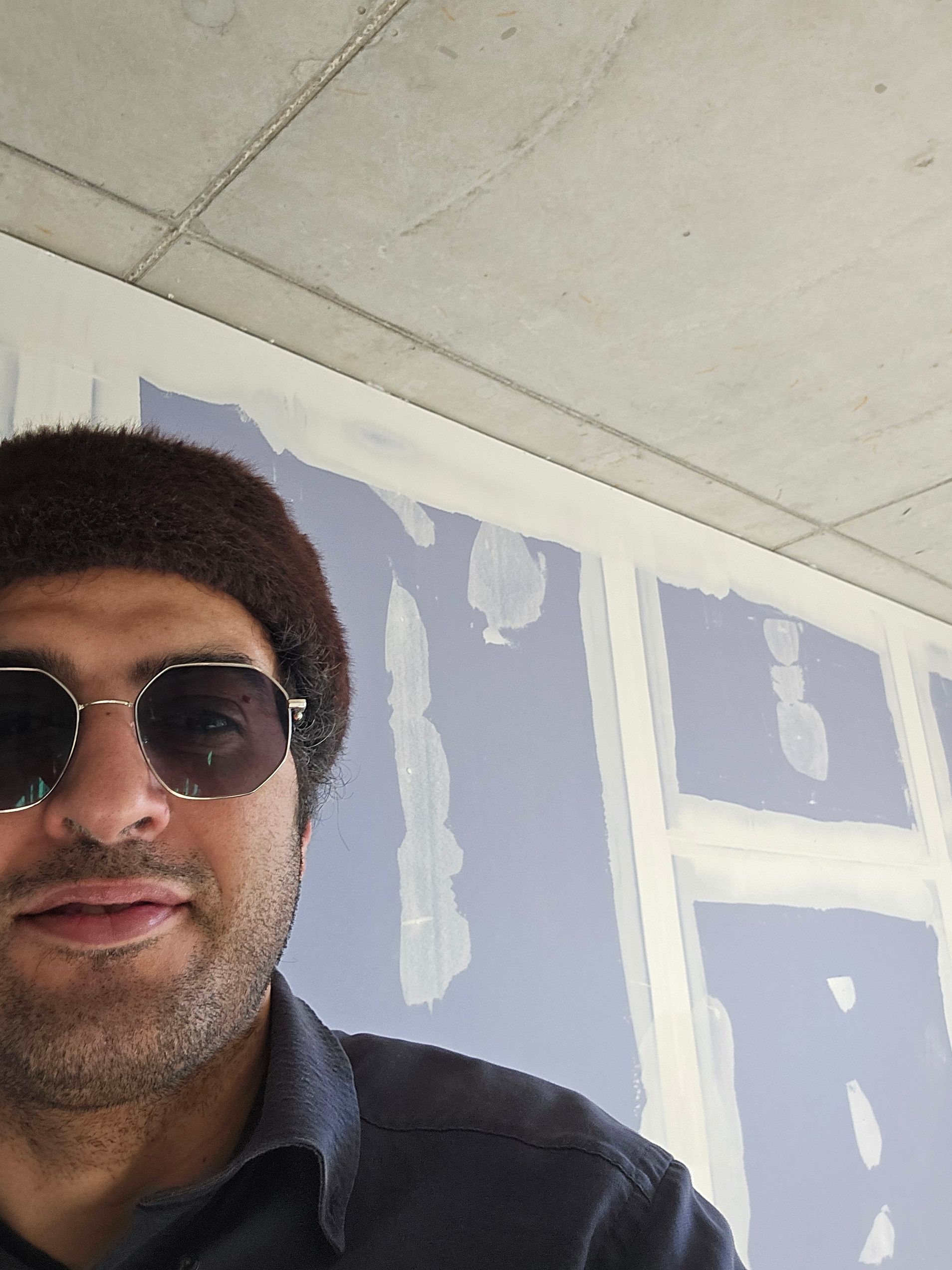 Ein Mann mit Sonnenbrille und Hut steht an einer Mauer. Die Mauer scheint im Bau zu sein.