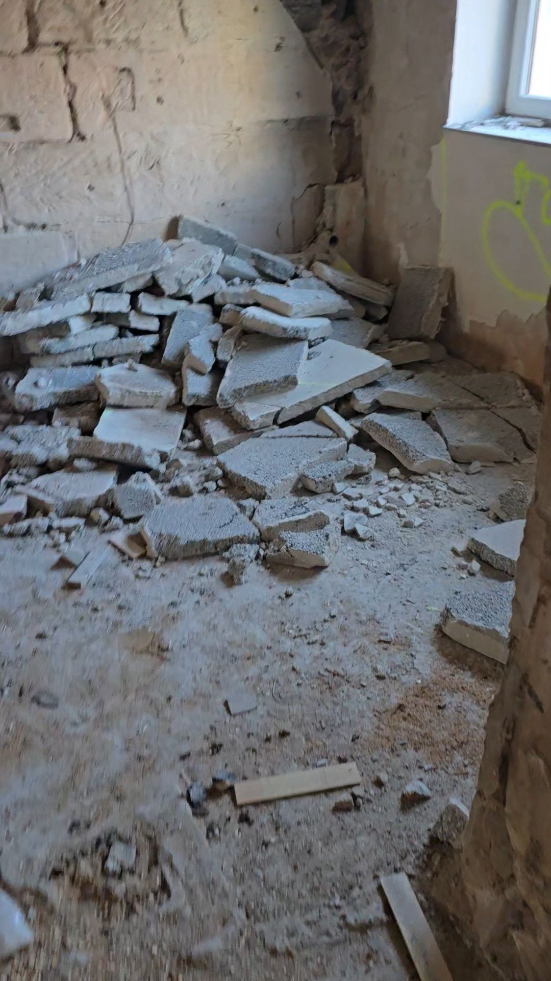 Ein Zimmer mit einem Haufen zerbrochener Betonplatten auf dem Boden in der Nähe eines Fensters.