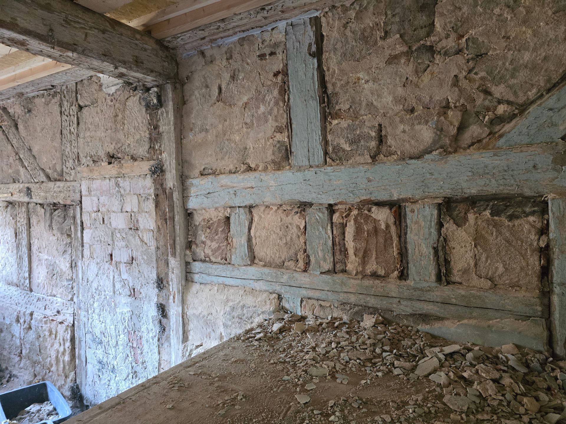 Innenansicht einer Mauer aus Stein und Fachwerk, davor blaue Balken und ein Schutthaufen.