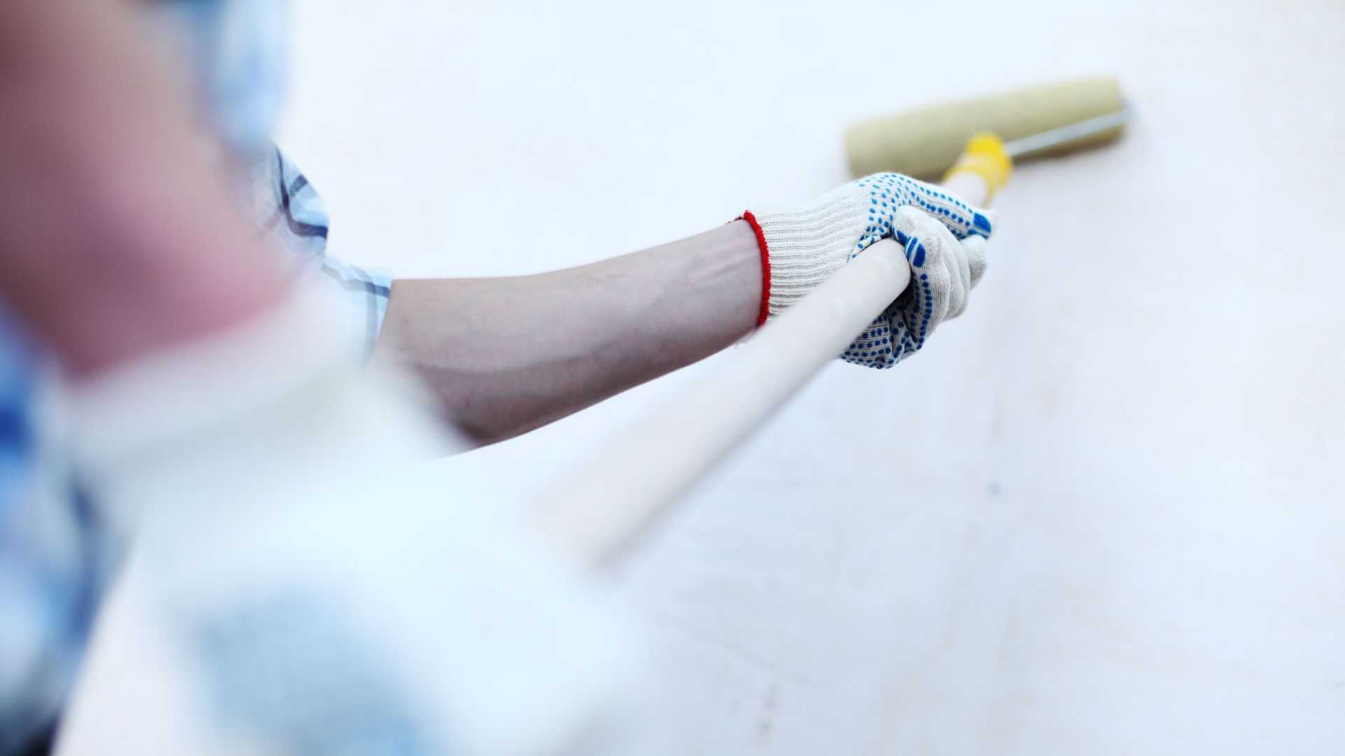 Person, die mit einer Farbrolle eine weiße Wand streicht.