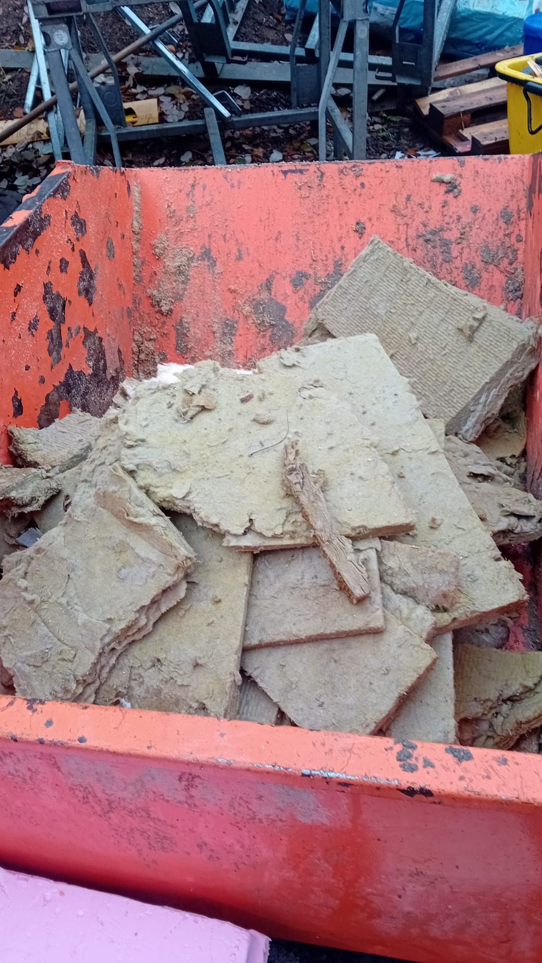 Ein orangefarbener Abfallcontainer, gefüllt mit zerbrochenen, hellbraunen Fliesen.