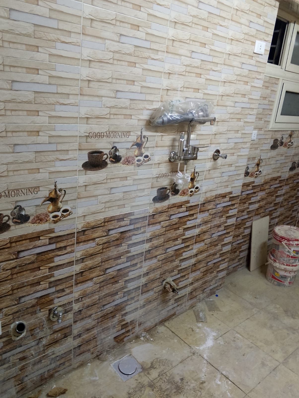 Geflieste Küchenwand mit Akzenten im Kaffee-Design. Braune und beige Strukturfliesen. Spüle und Wasserleitungen sind sichtbar.