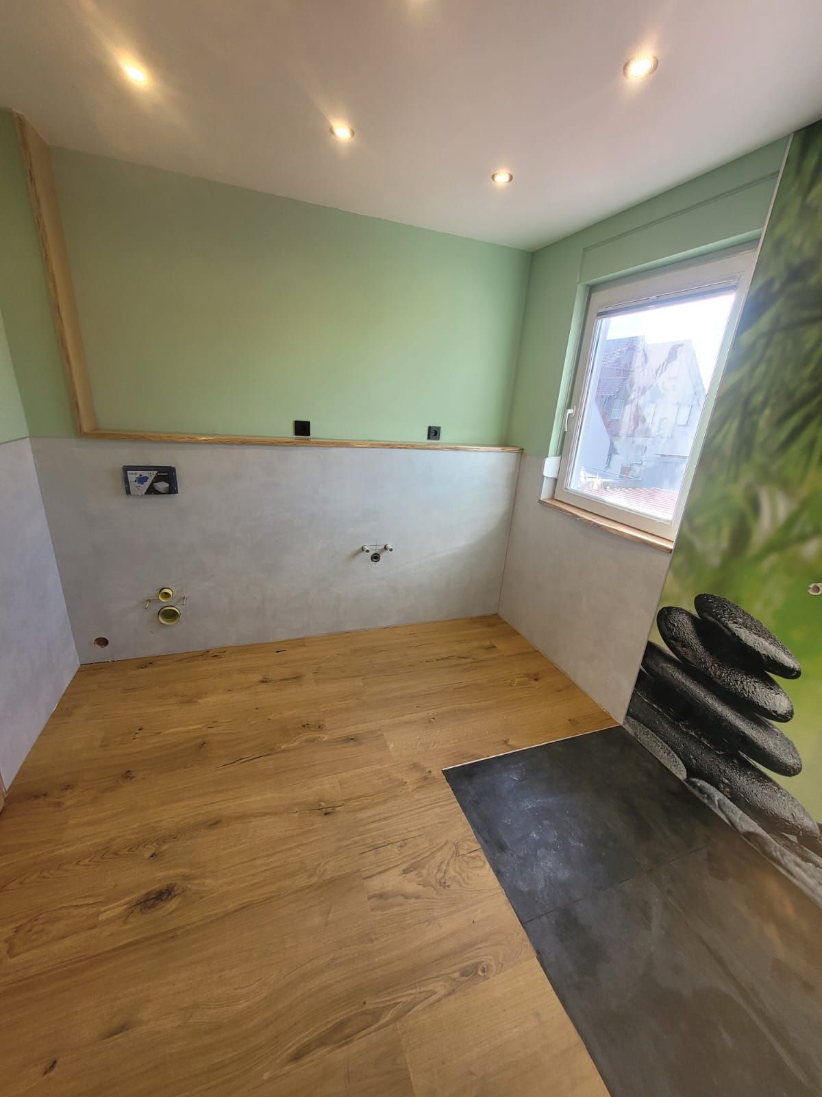 Badezimmer mit hellem Holzboden, grünen und grauen Wänden, kleinem Fenster und Wandgrafik im Zen-Stil.