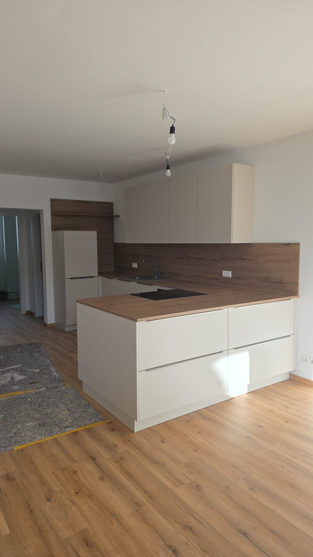 Moderne Küche mit hellen Schränken, Arbeitsplatten aus Holz, Kochinsel und Fliesenspiegel. Der Raum ist lichtdurchflutet.