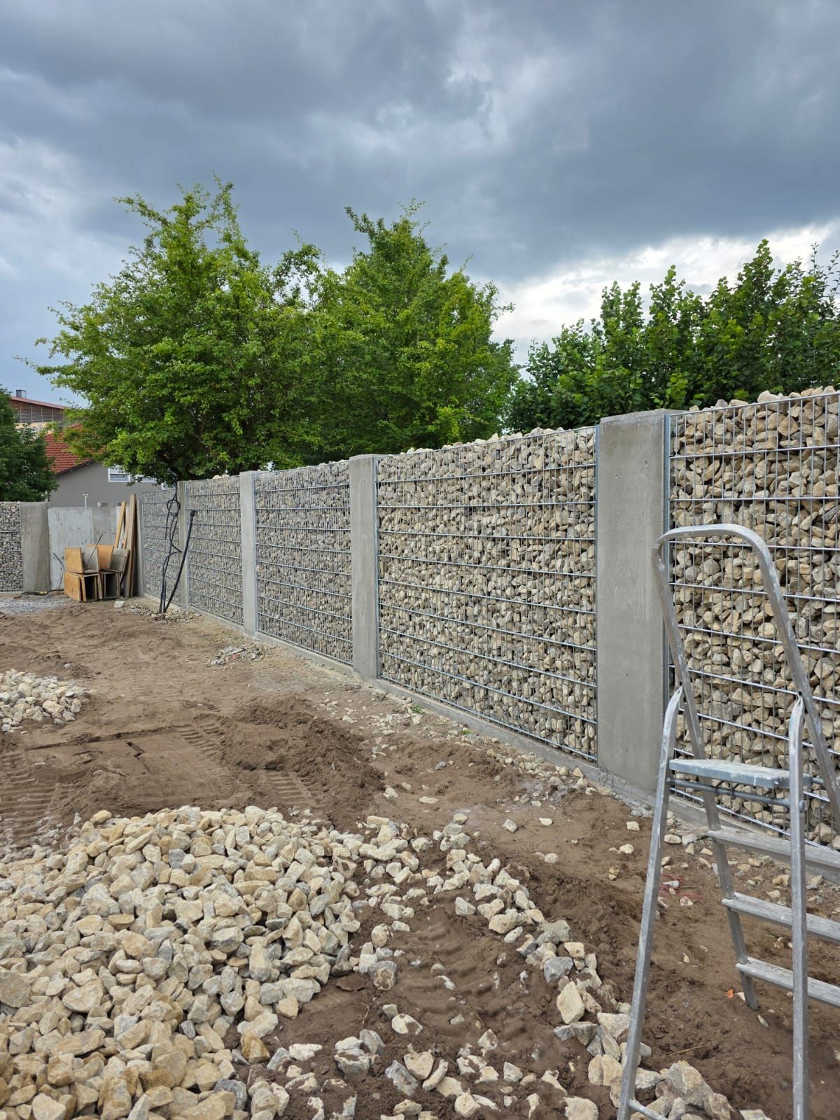 Ein im Bau befindlicher Gabionenzaun aus Stein und Beton an einem bewölkten Tag.